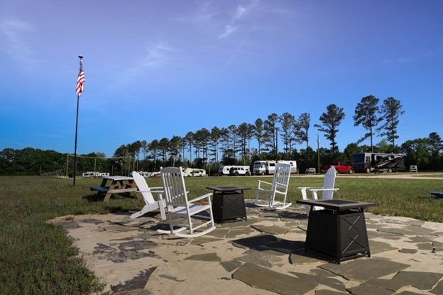 Outdoor patio with white rocking chairs and tables on a stone pad, an American flag flying nearby.