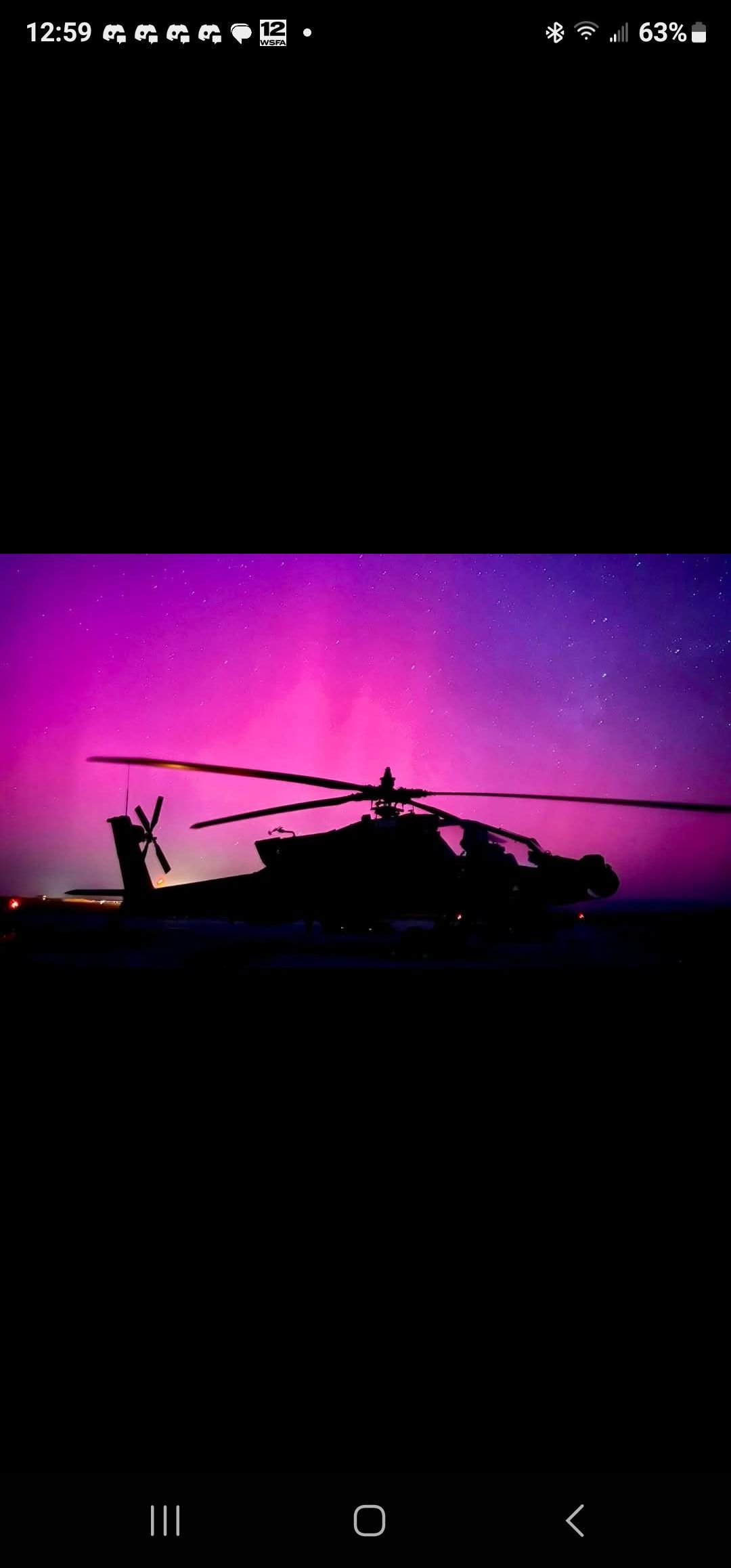 Silhouette of a helicopter flying against a purple-pink sunset sky with a small moon above.