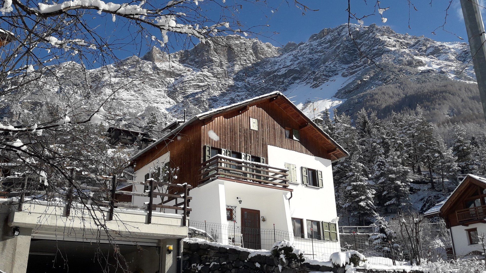 Una casa è circondata da alberi innevati e montagne sullo sfondo.