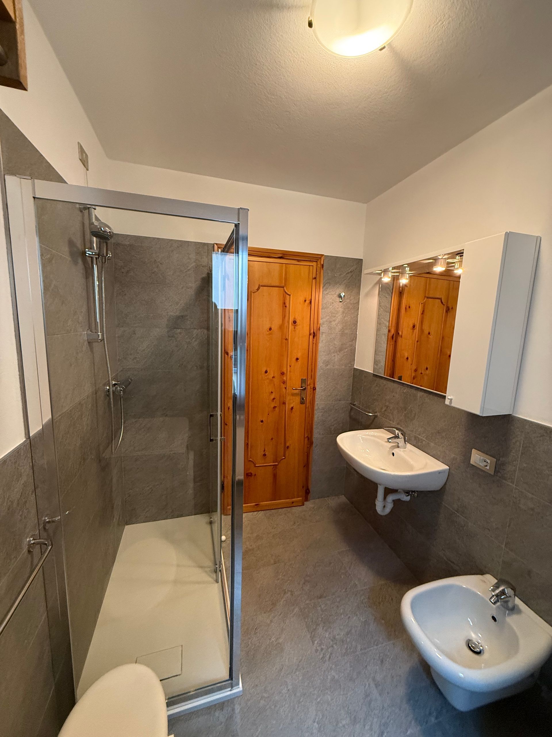 Un bagno con lavandino, water, doccia e specchio.