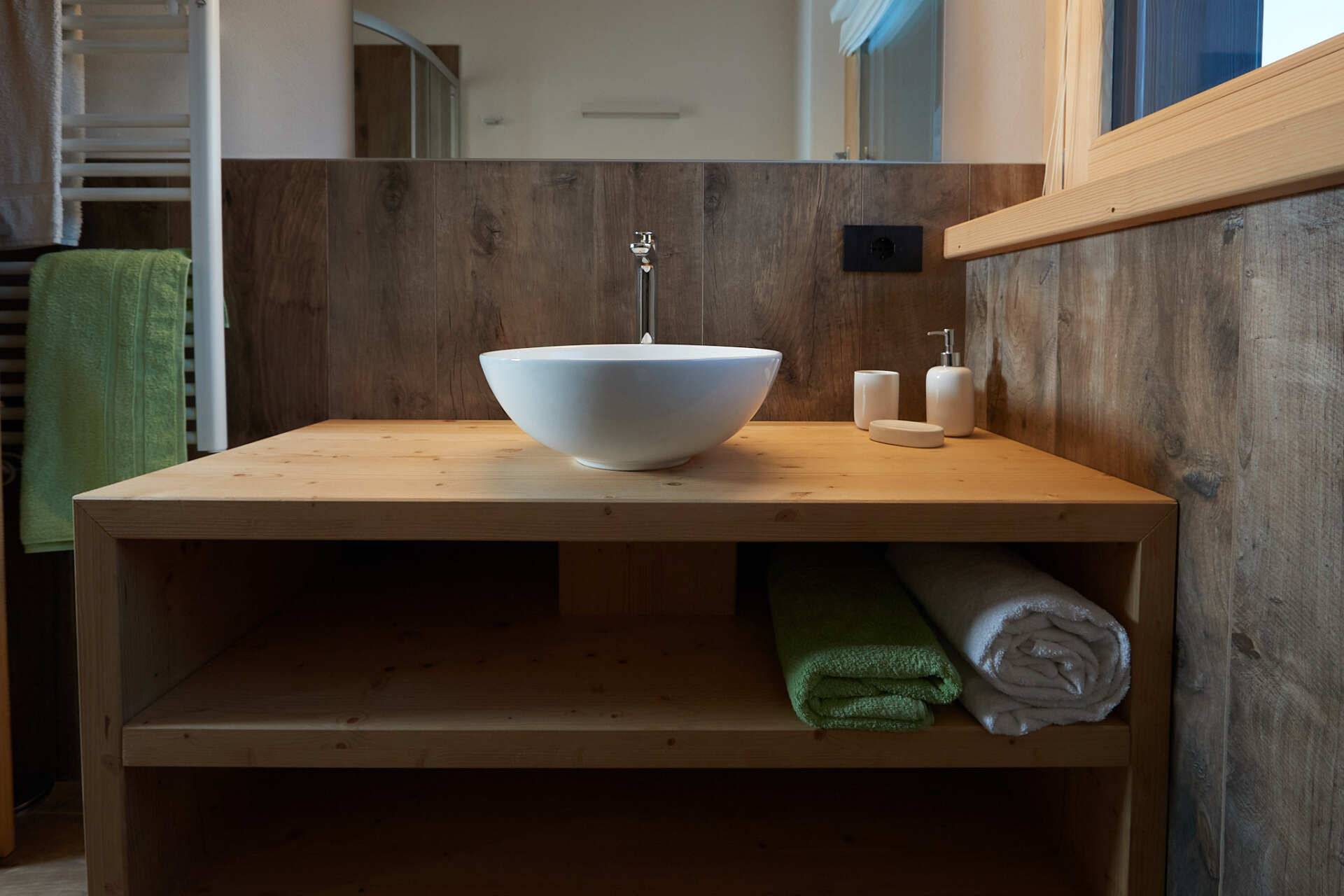 Un bagno con lavandino e asciugamani su un ripiano di legno.
