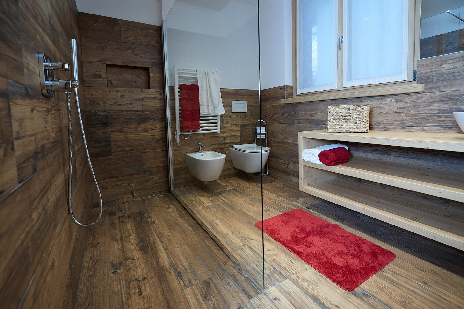 Un bagno con pavimenti in legno, un water, un bidet e un tappeto rosso.