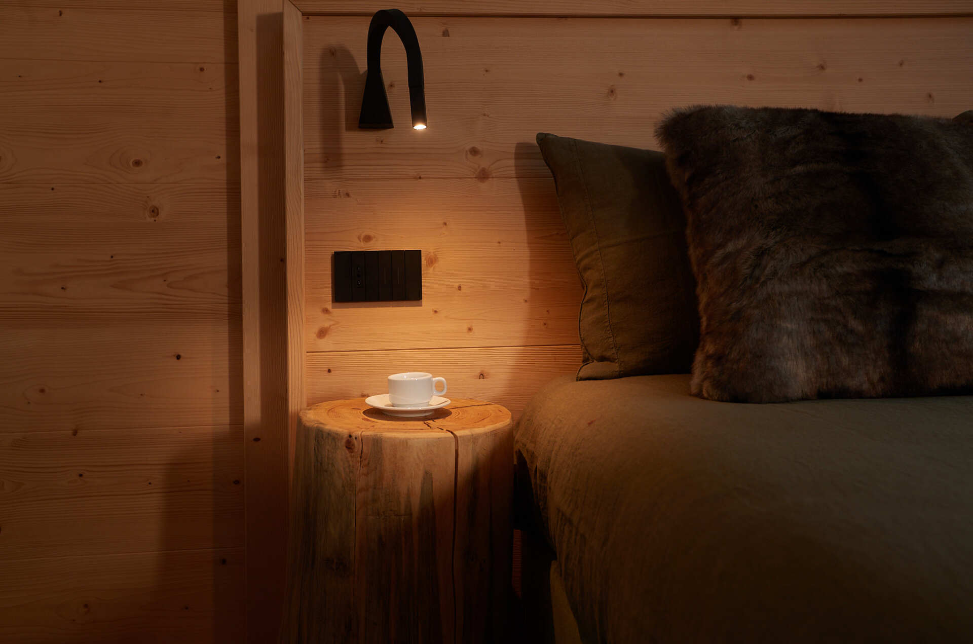 Un letto con testiera in legno e un comodino in legno con una tazza di caffè sopra.