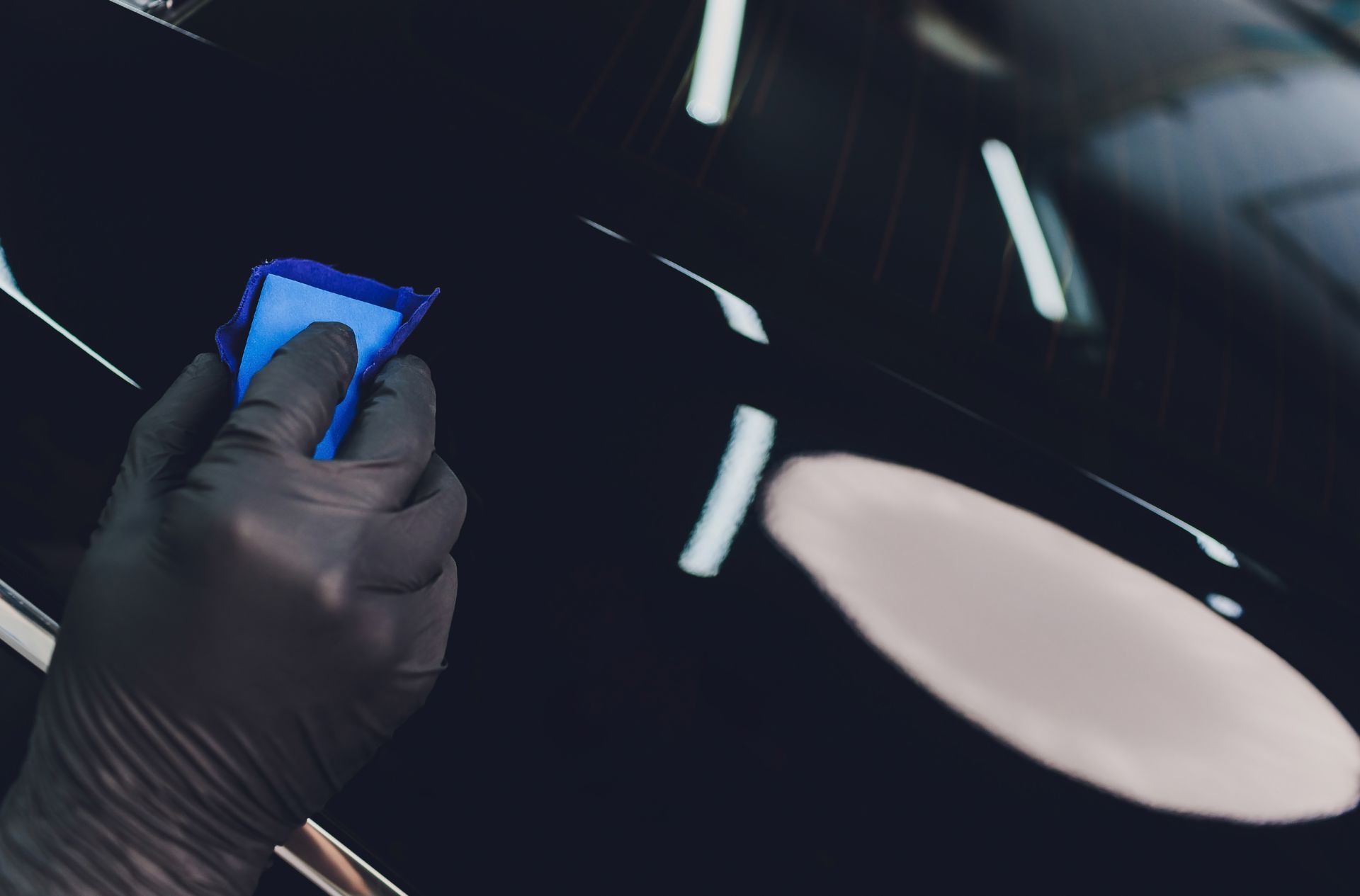 A person is holding a blue object in their hand in front of a car.