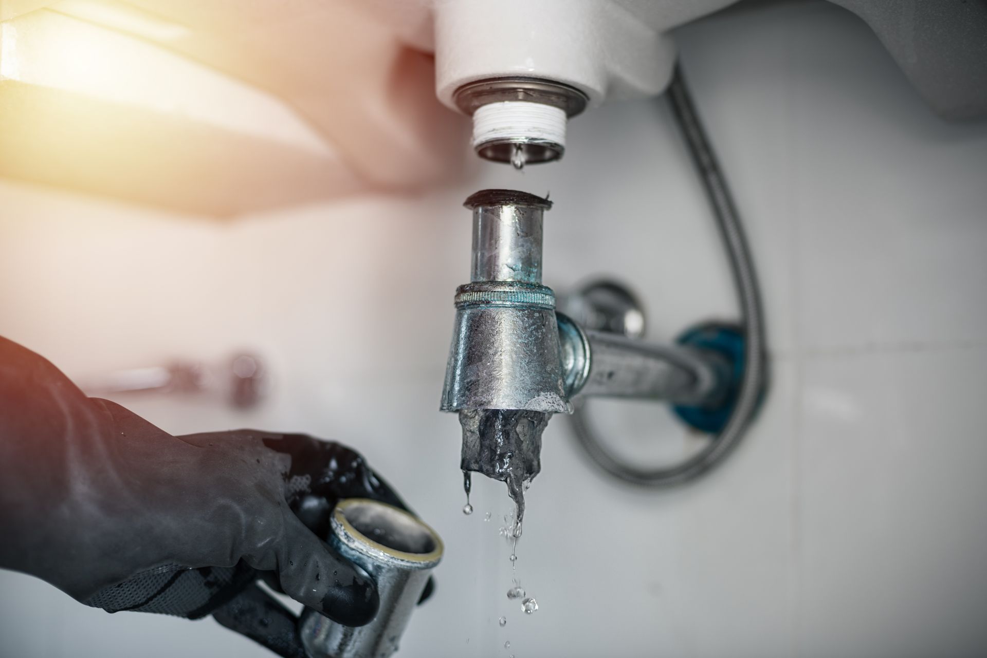 A plumber is fixing a leaking sink pipe in a bathroom.