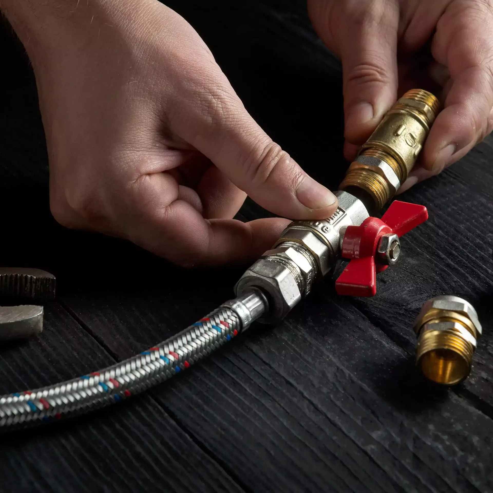 Person assembling plumbing with a red valve on dark wood.