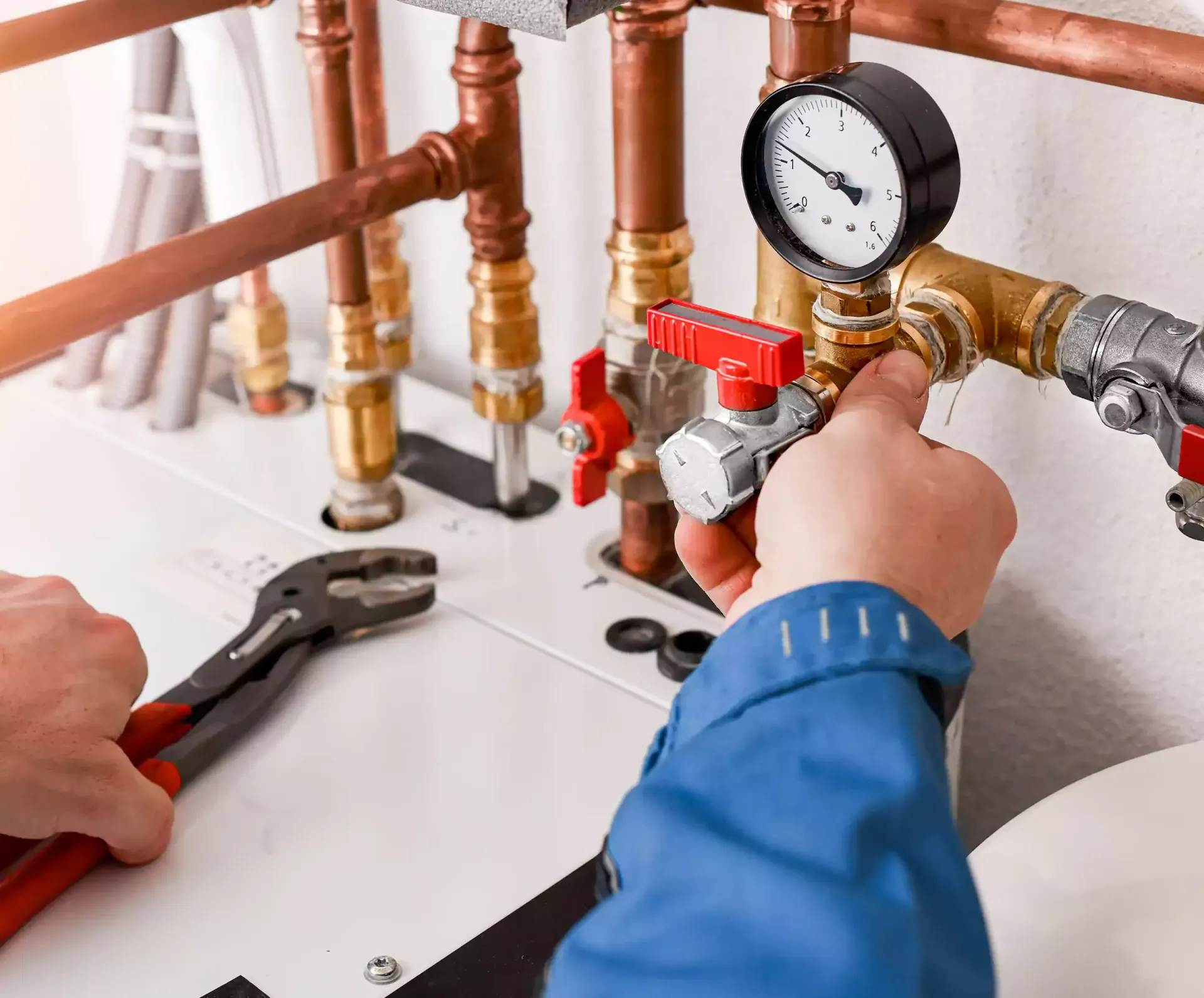 Plumber working on copper pipes, turning a valve with a pressure gauge. A wrench is on the left.
