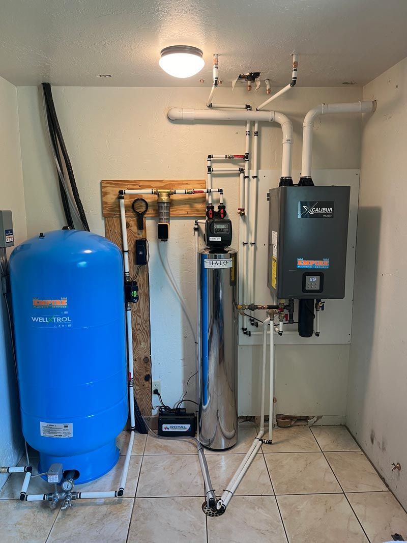 Water heater and water treatment system in a utility room. Blue pressure tank, silver filter, and gas heater.