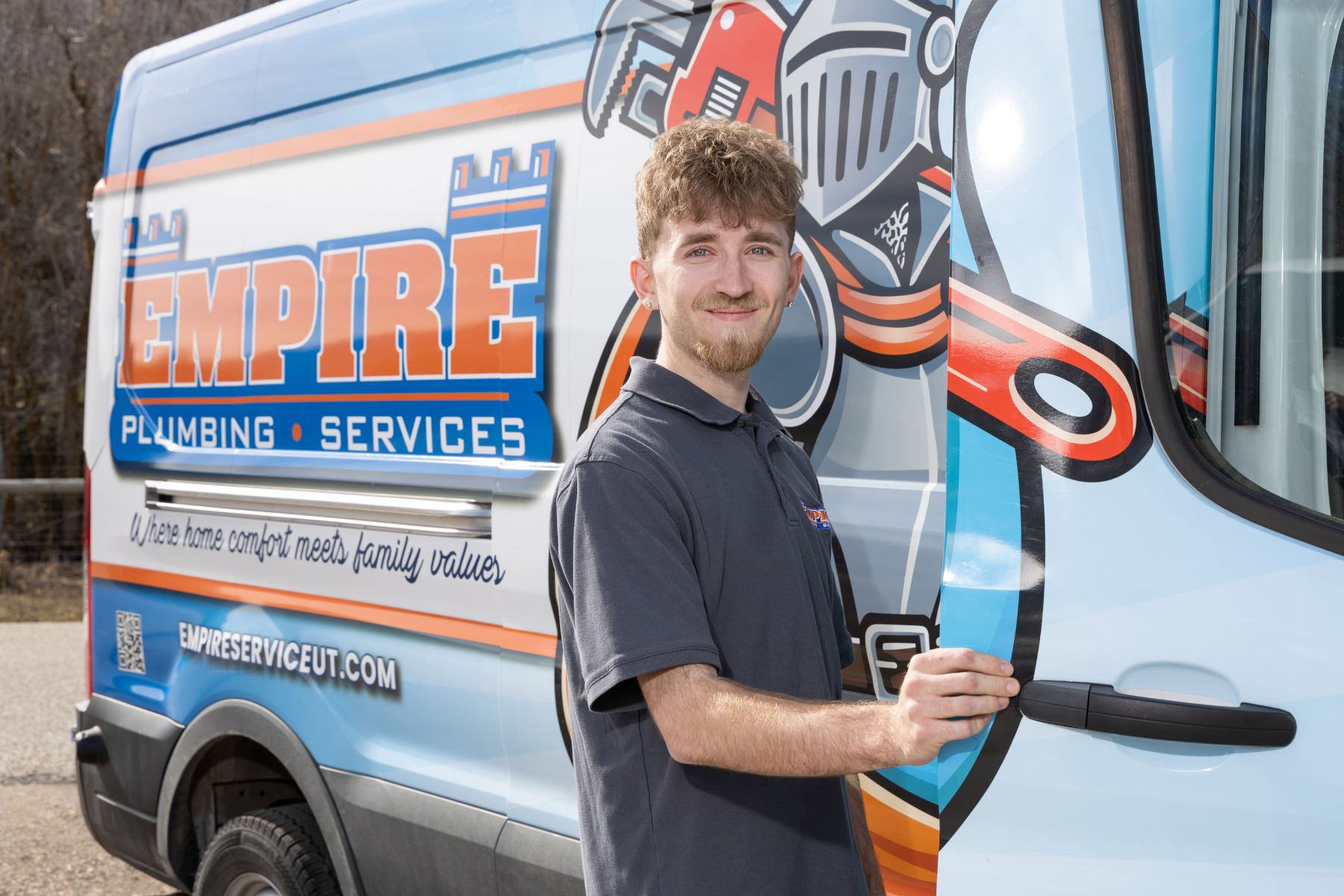 Plumber in blue uniform fixing pipes under a sink with tools beside him.