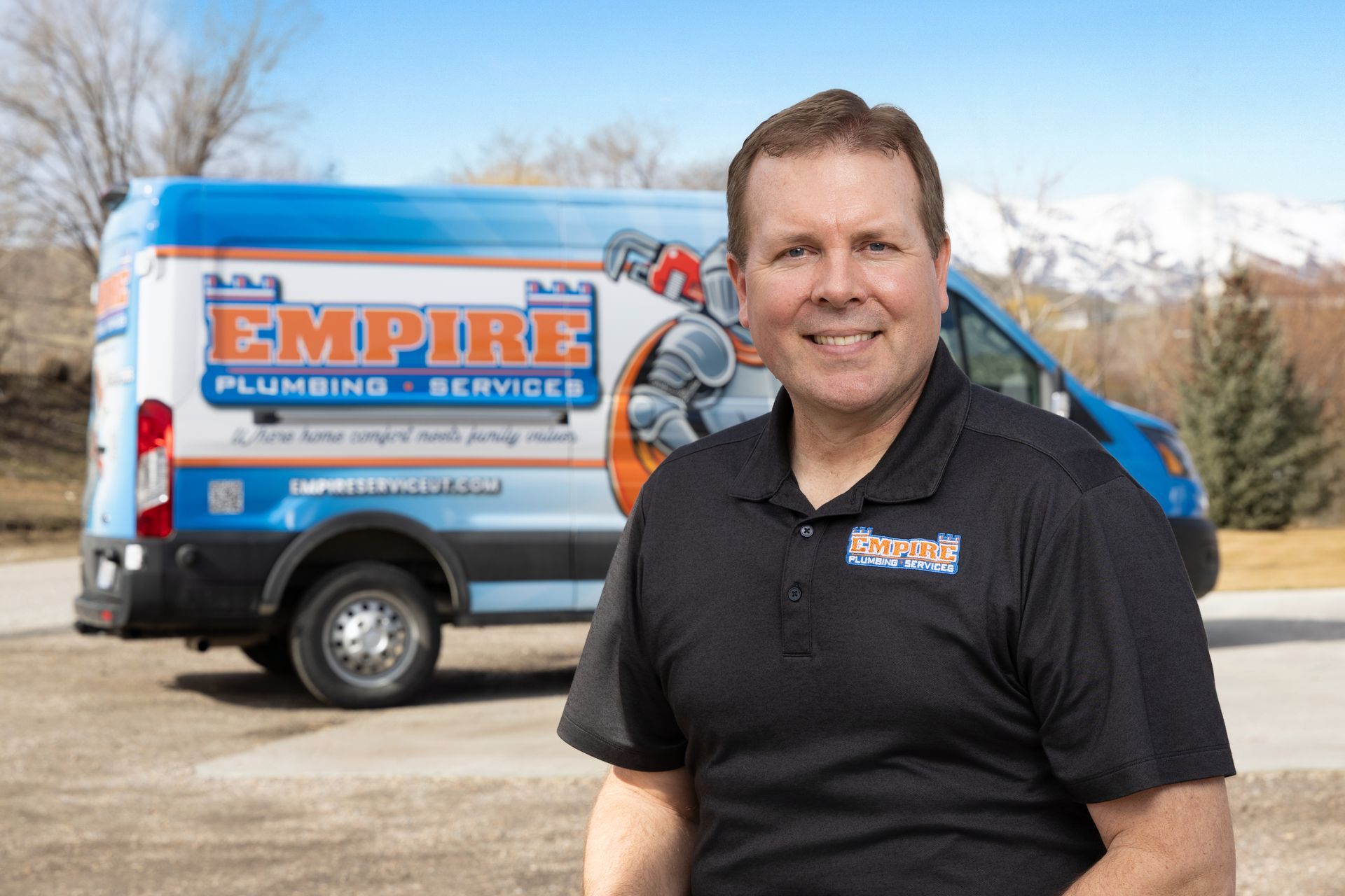 Man in black polo standing in front of a blue Empire Plumbing & Service van outdoors