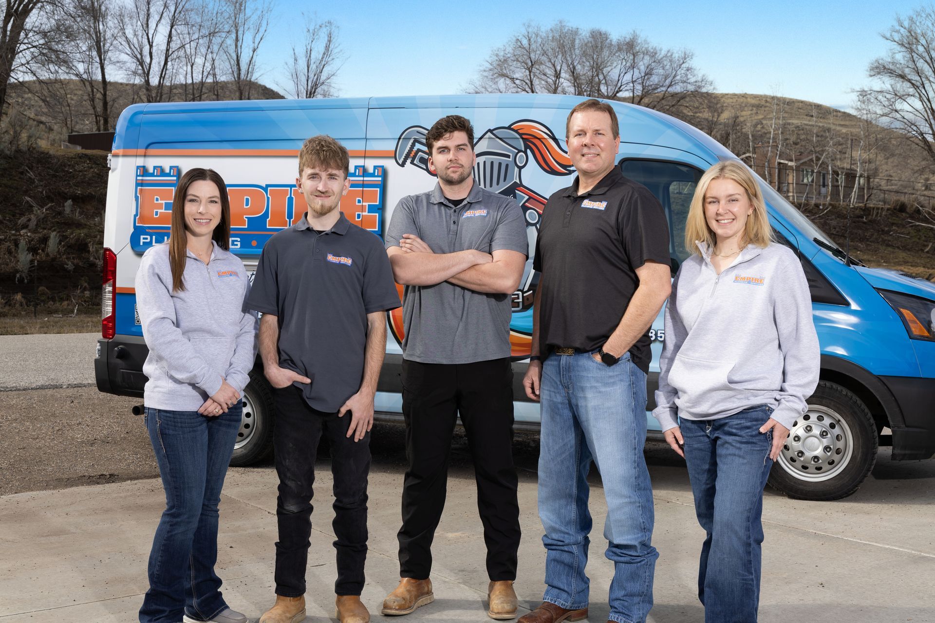 Five people standing in front of a blue van with orange lettering on a roadside.