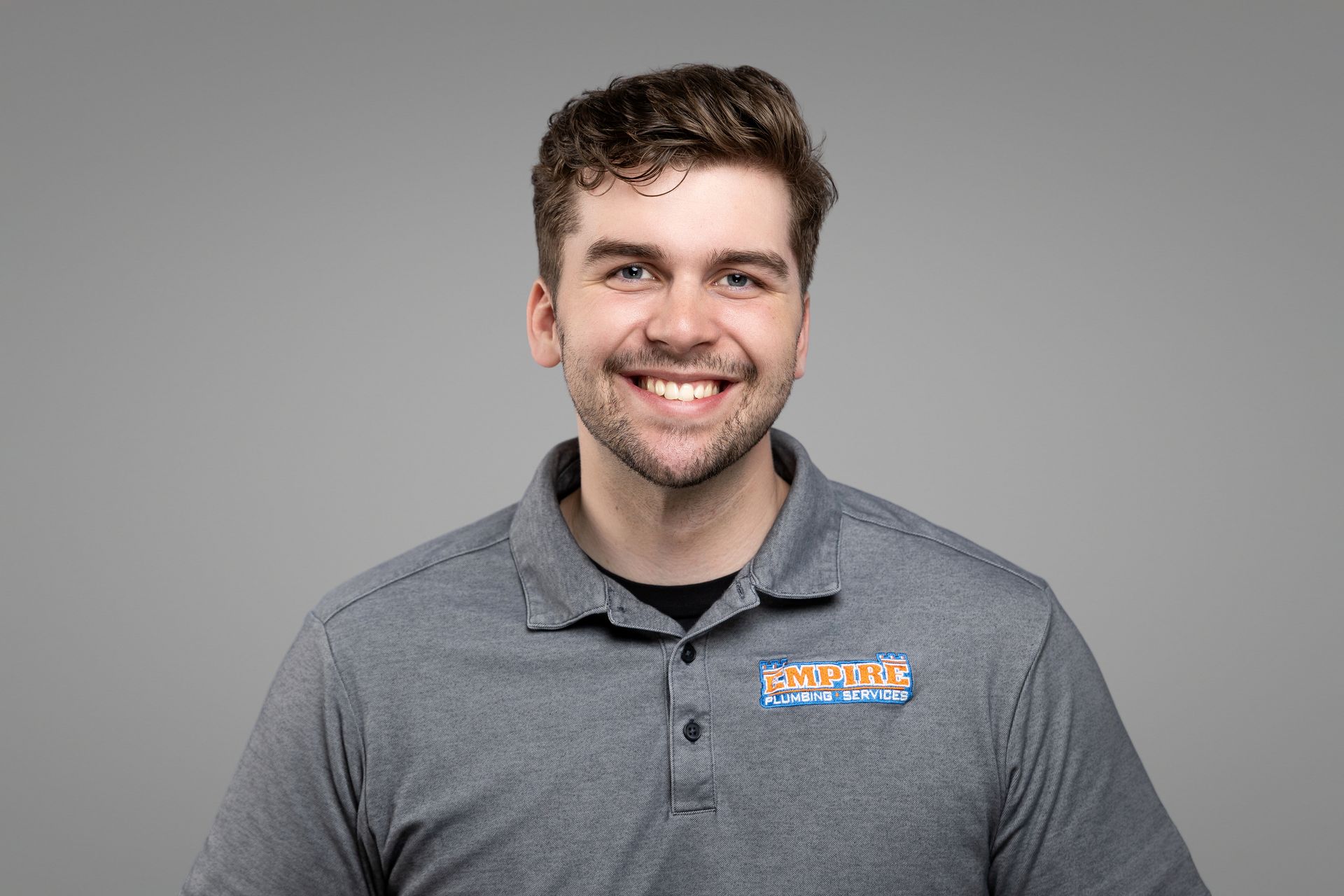 Smiling man in a gray polo shirt against a plain gray background