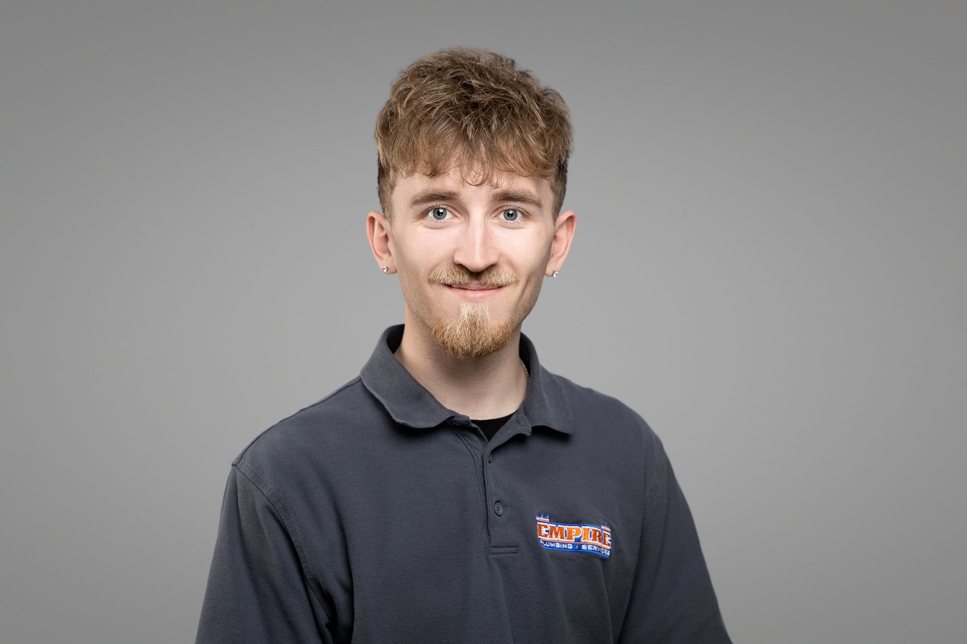 Smiling man in a dark polo shirt against a plain gray background