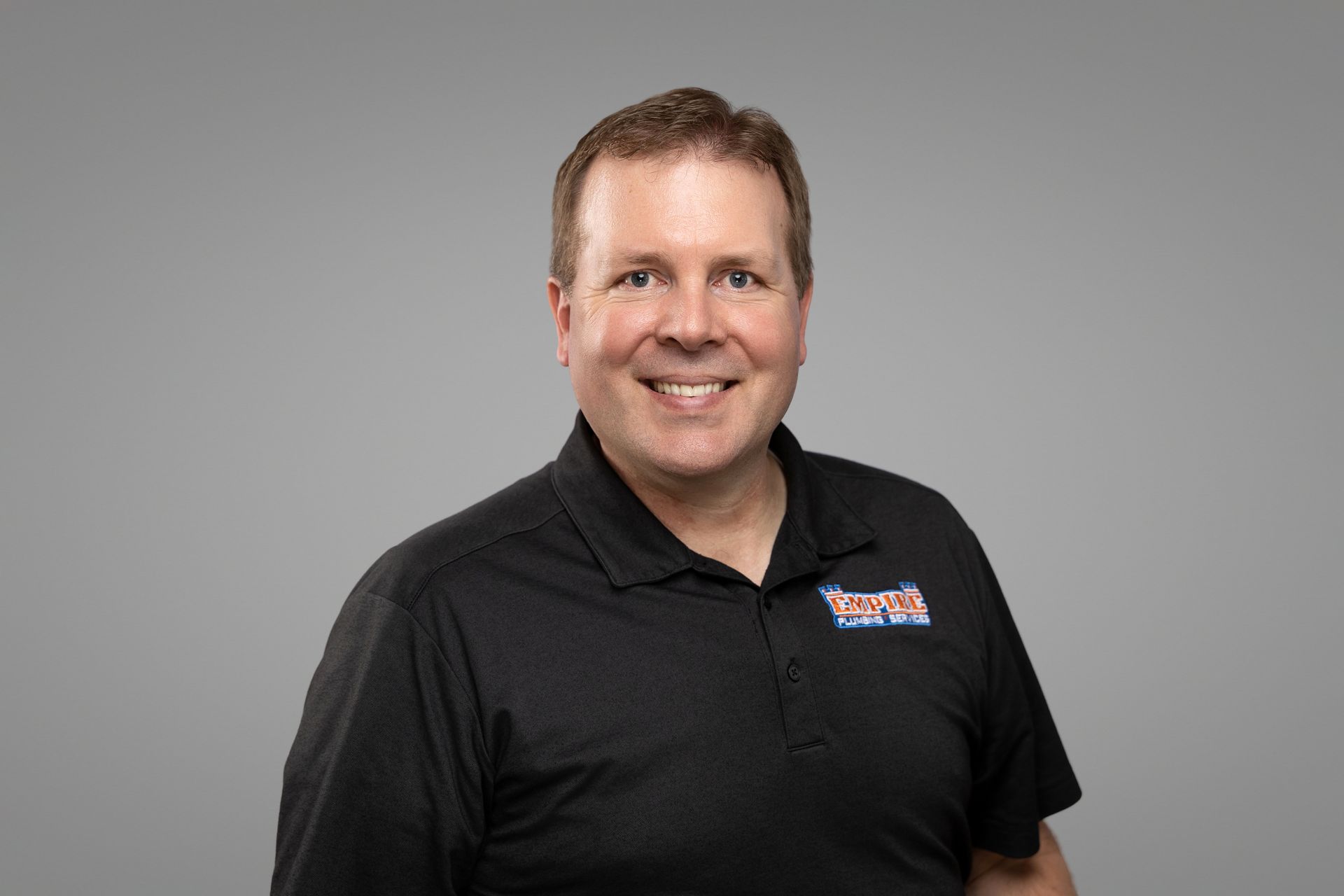 Smiling man in a black polo shirt against a plain gray background