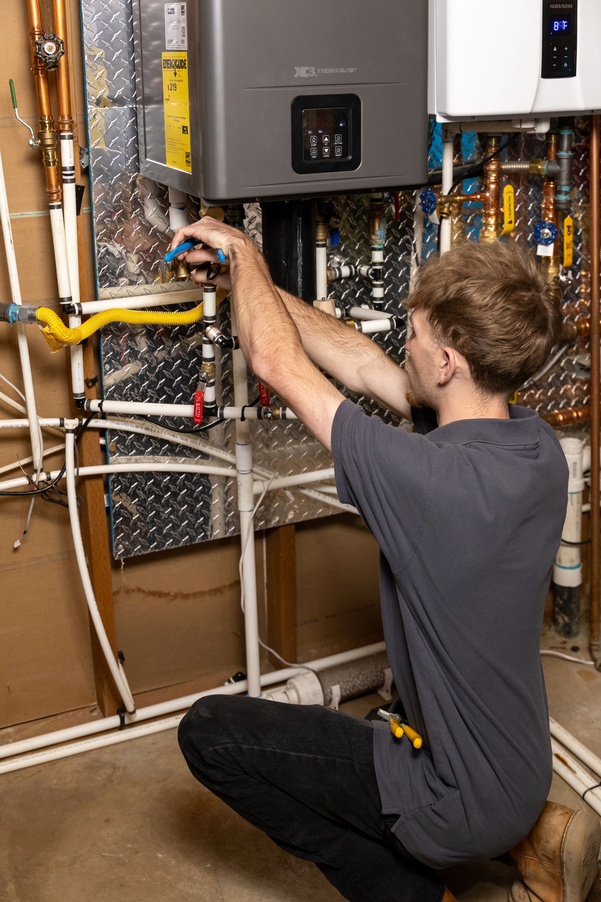 Technician kneeling beside a wall-mounted HVAC unit, working on exposed wiring in a utility room.