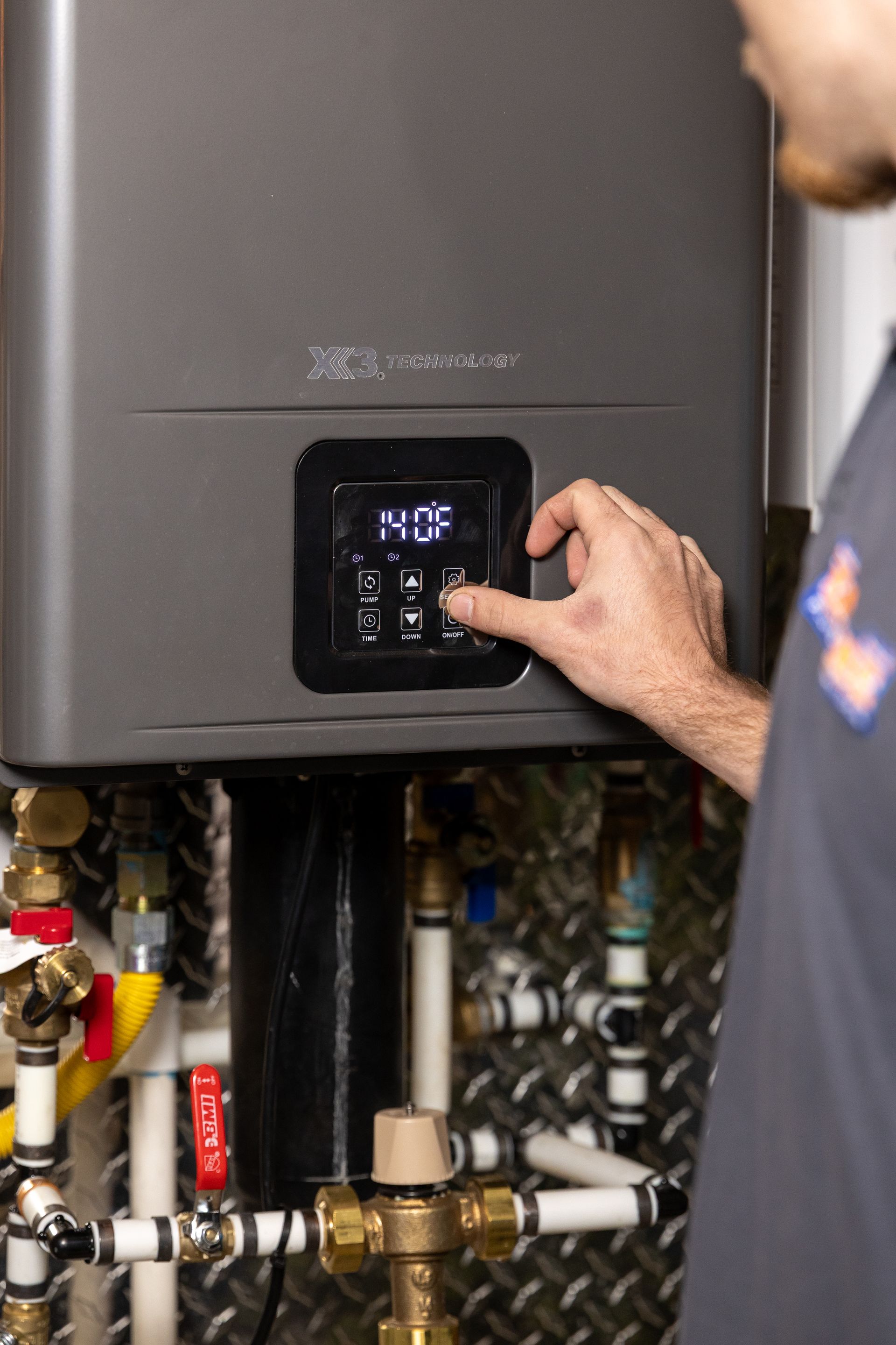 Person adjusting the control panel on a gray boiler unit in a mechanical room.