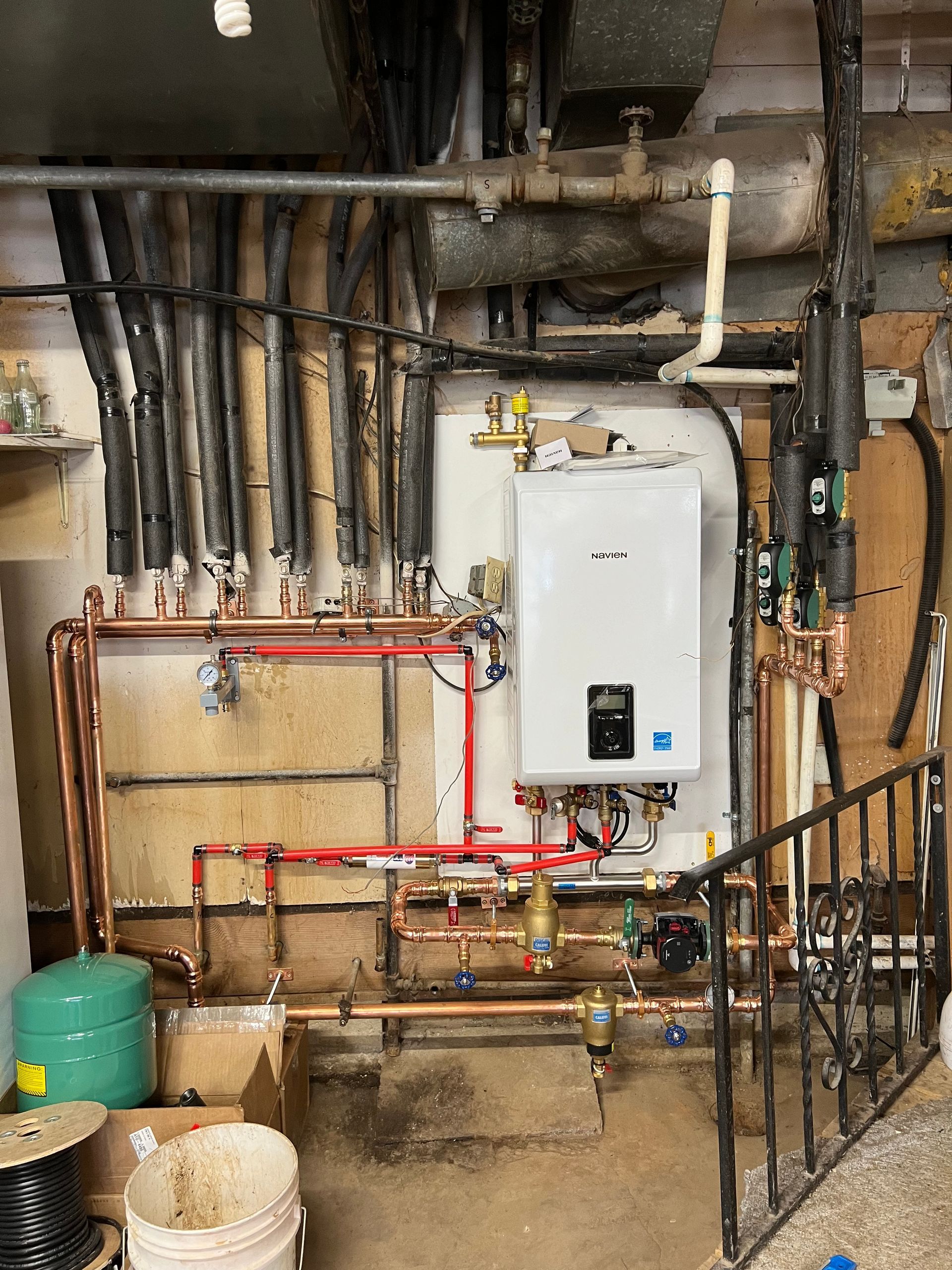 A gas-powered water heater installed in a basement, connected to copper pipes and heating system.