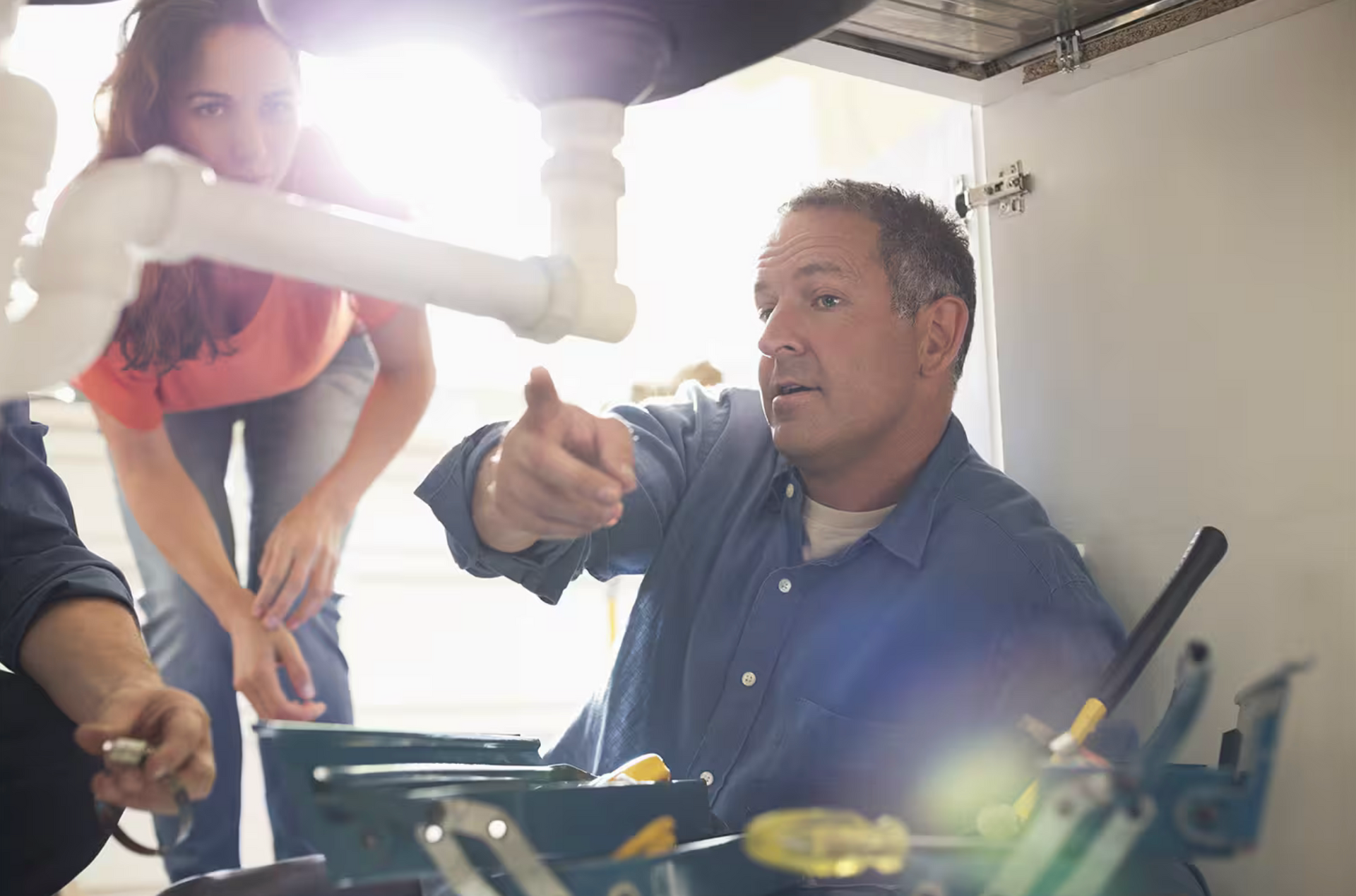 A man is showing a water flows in a kitchen sink while a woman looks on.