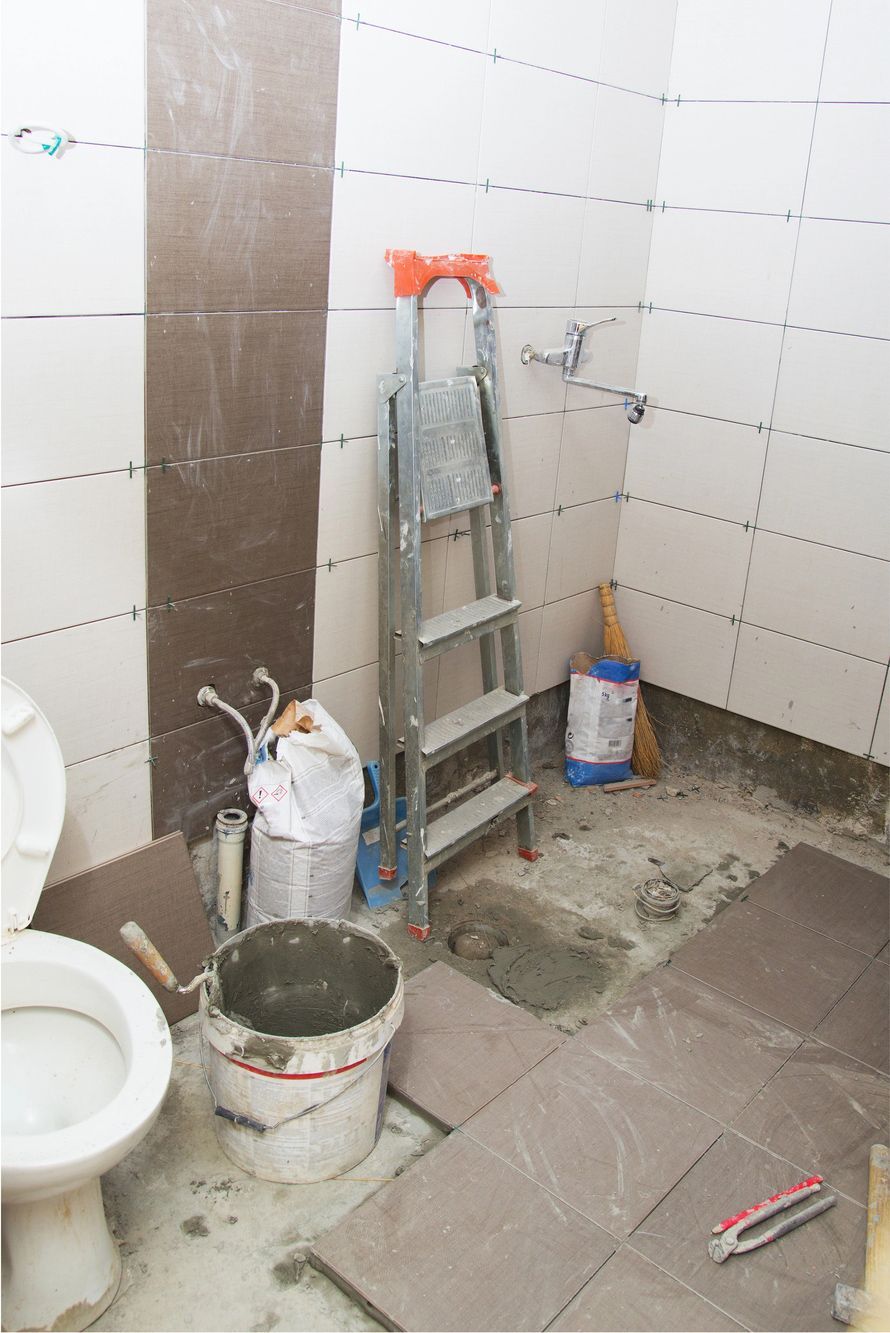 Tiled bathroom under renovation with ladder, buckets, and tools on the floor.