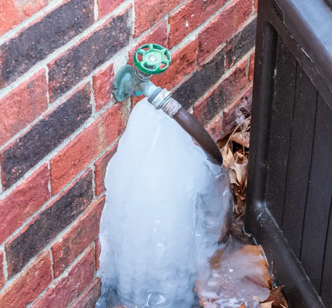 Ice on the siding and patio below an outdoor faucet that leaked after freezing