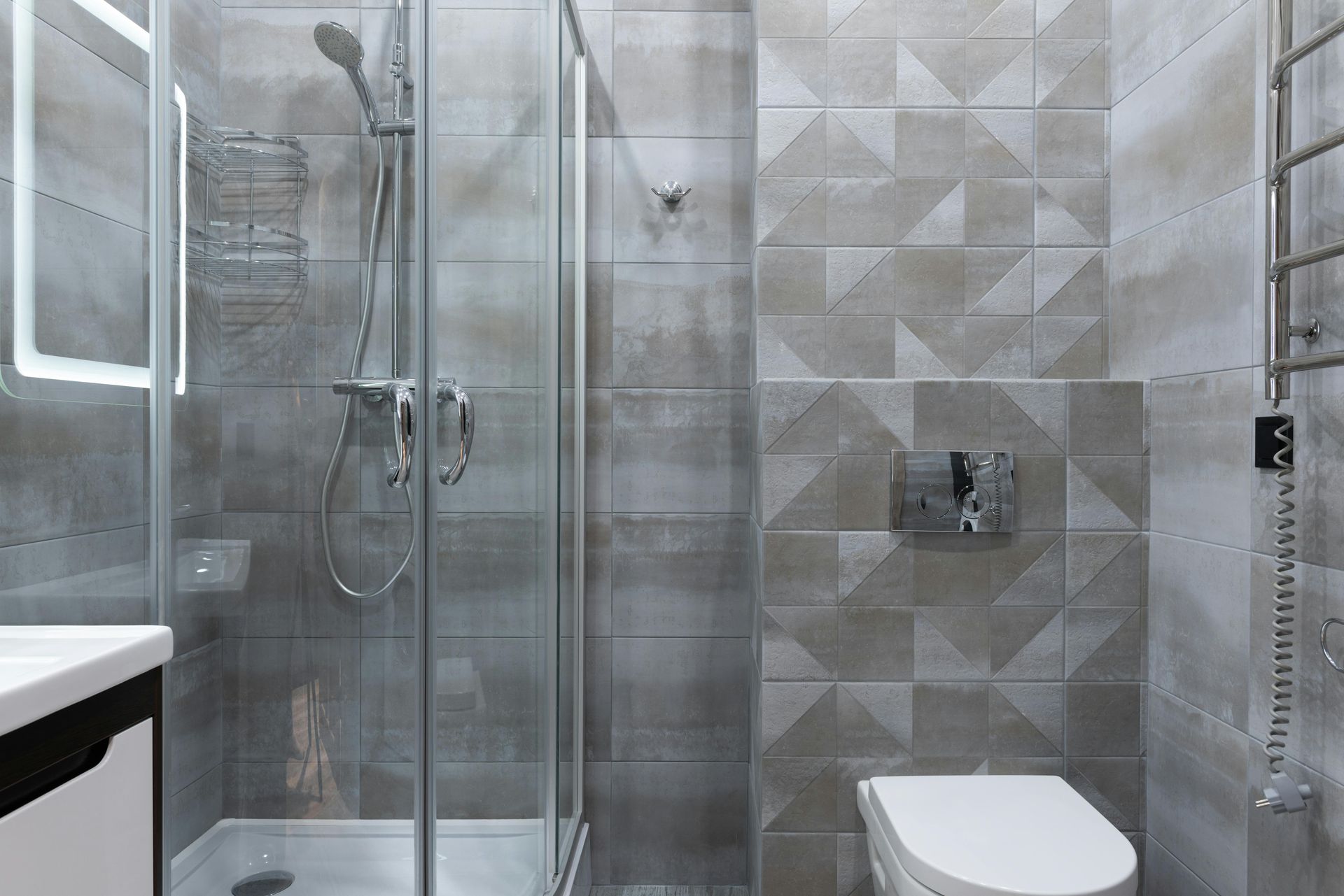 Modern bathroom with gray geometric tiles, a glass shower, and a white toilet.