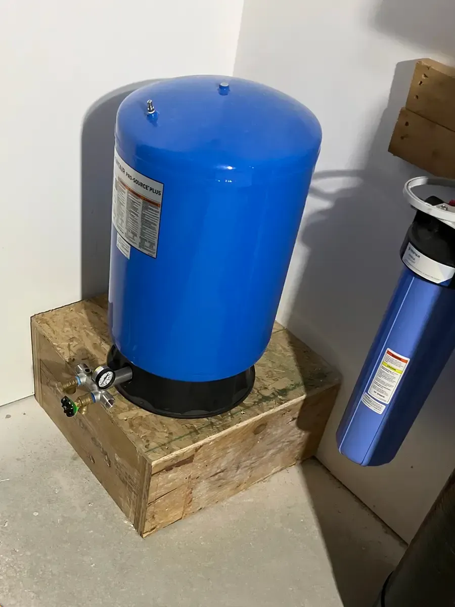 Water pressure tank with gauge and valves installed beside a whole-house filter