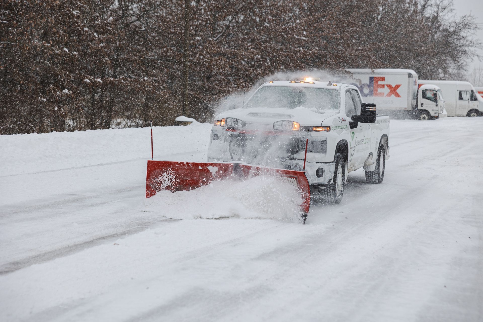 Snowplow clearing a snowy road with a FedEx truck behind it in heavy snowfall