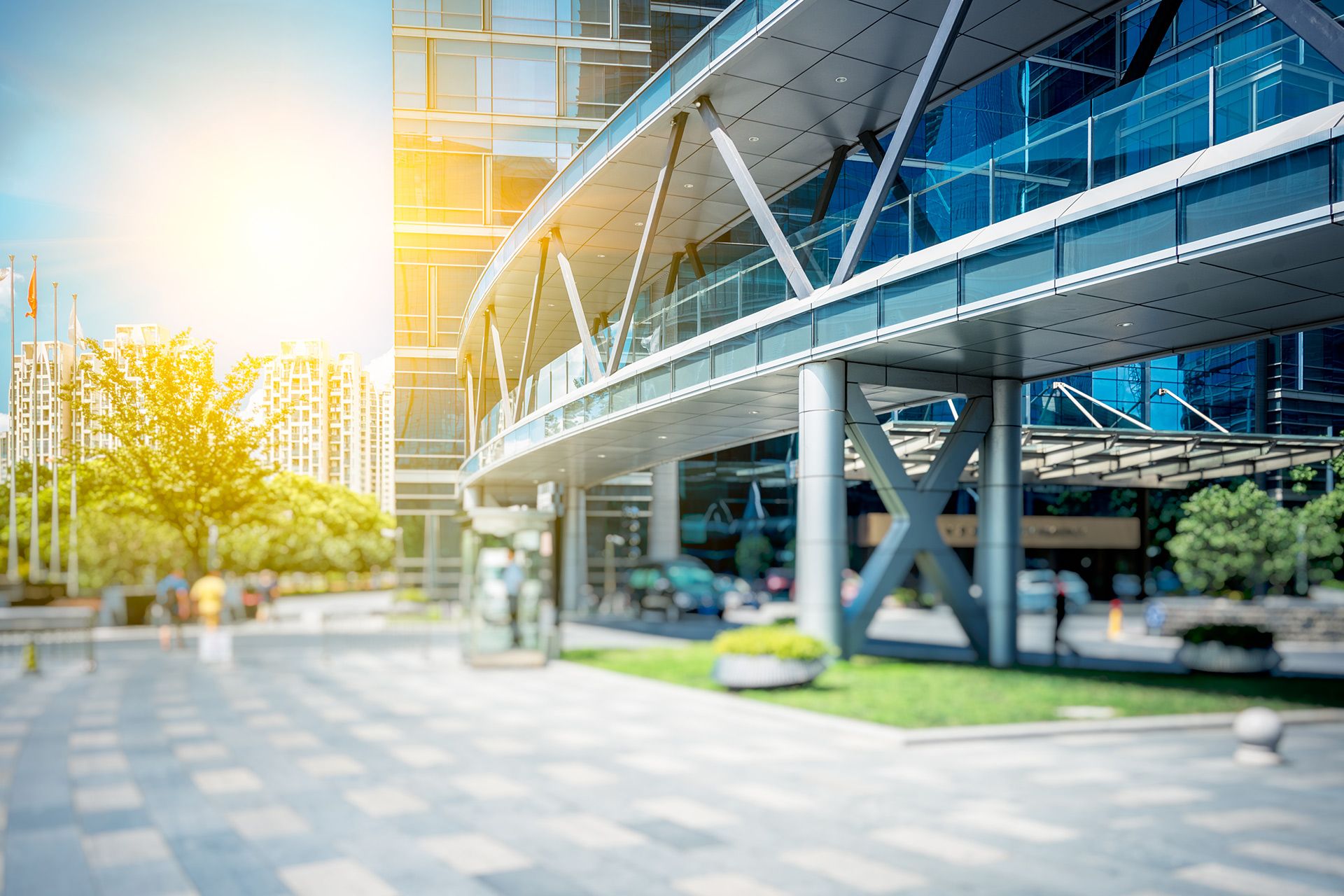 Modern glass office building with sunlit plaza and trees