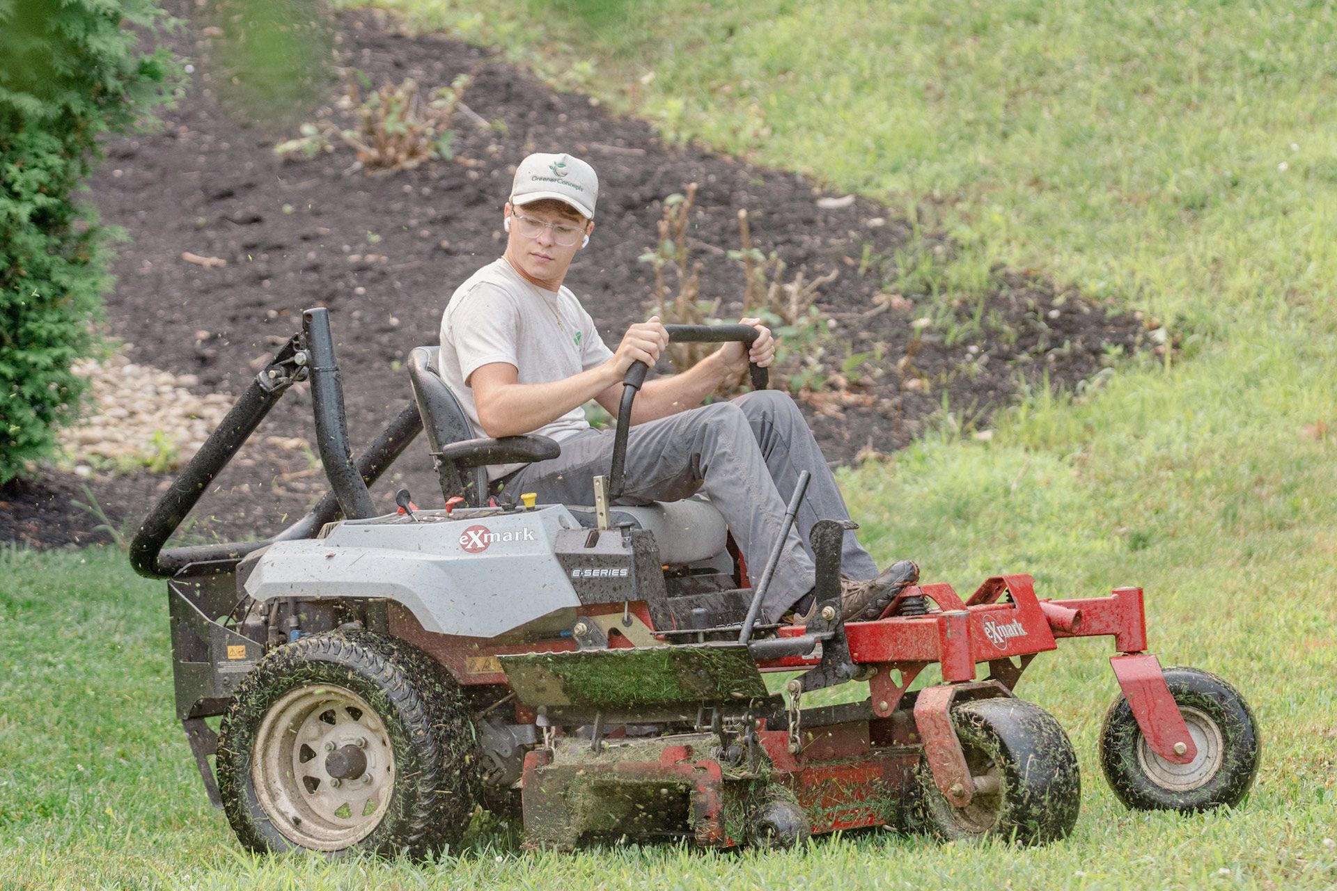 Person driving a gray lawn mower with red attachments across a grassy field