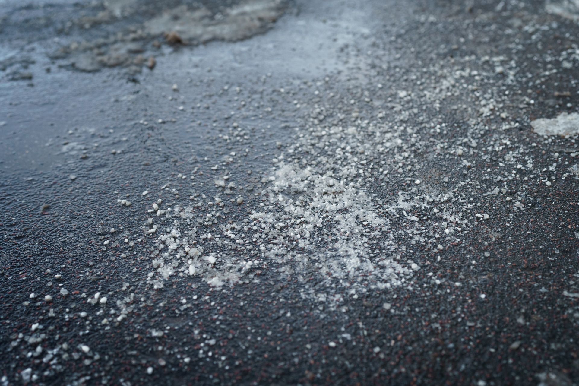 Icy, snow-dusted road surface with patches of white frost on dark pavement