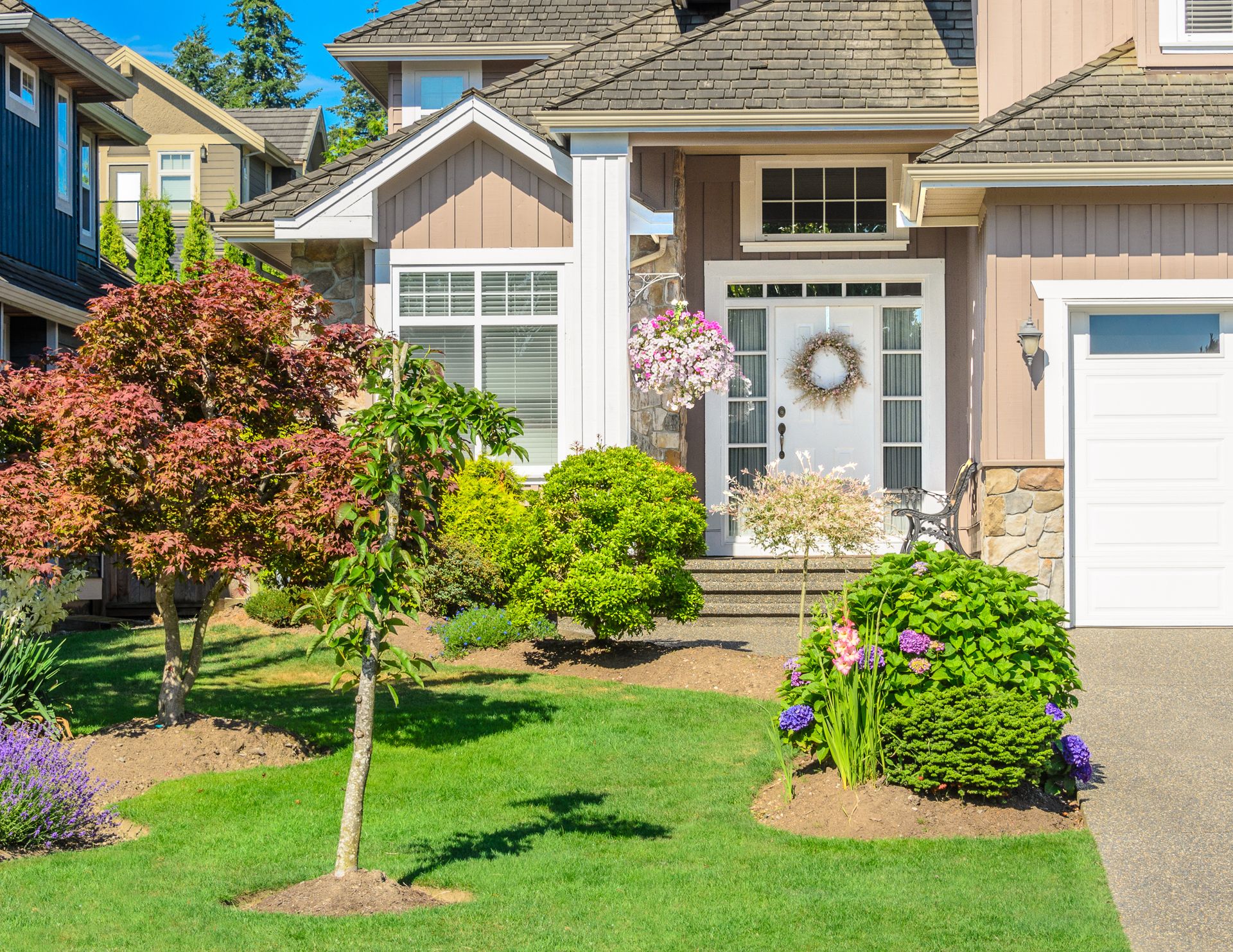 Suburban house front entrance with a wreath, small trees, and a green lawn in bright sunlight