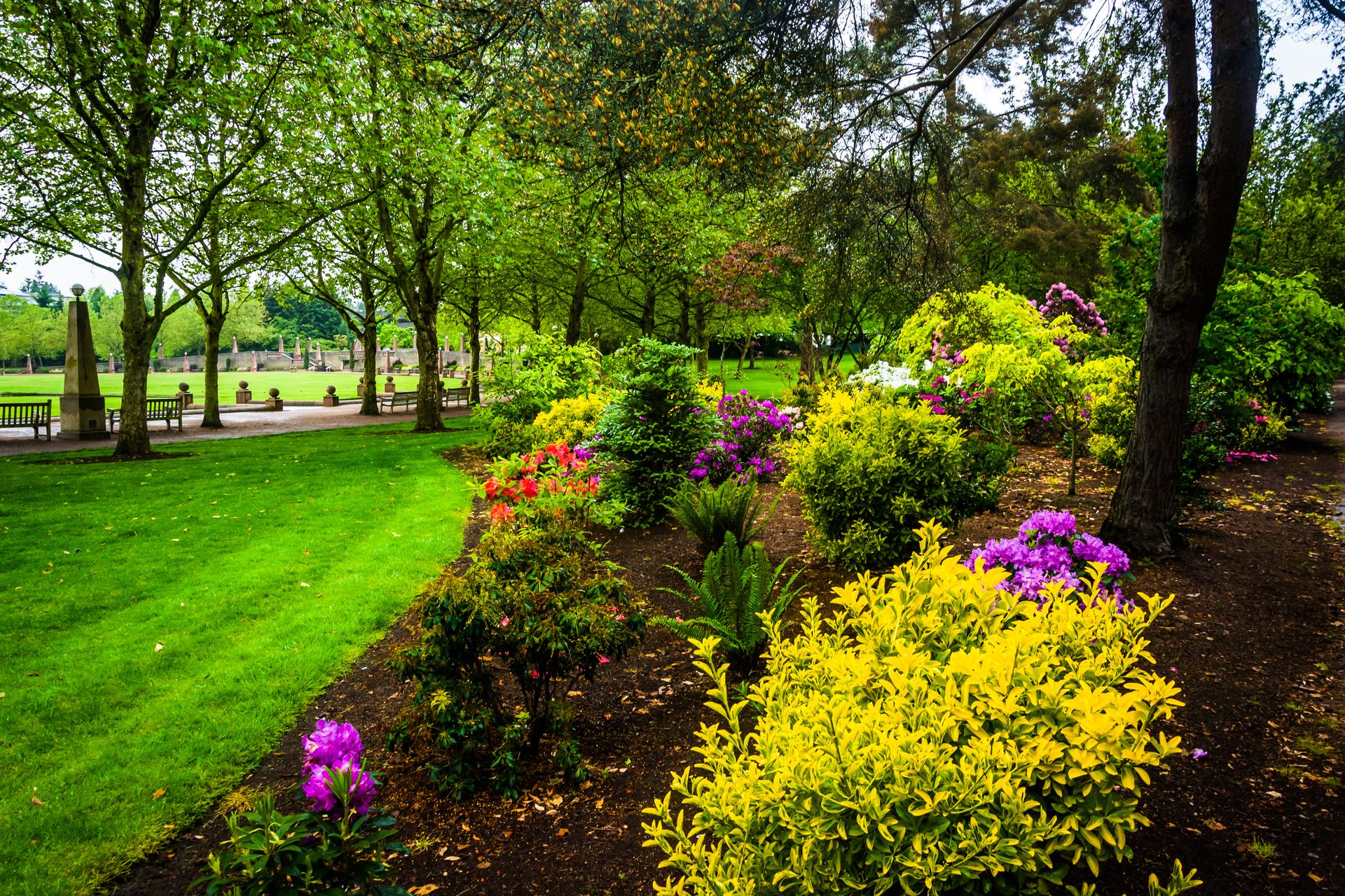 Colorful flower bed along a green park path with trees and grass
