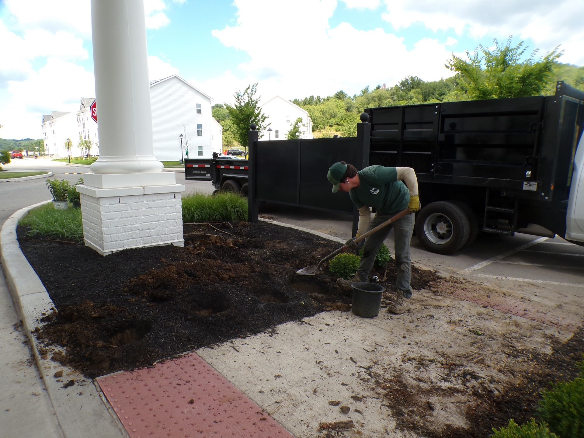 Worker planting in a landscaped area beside a black truck near a building entrance