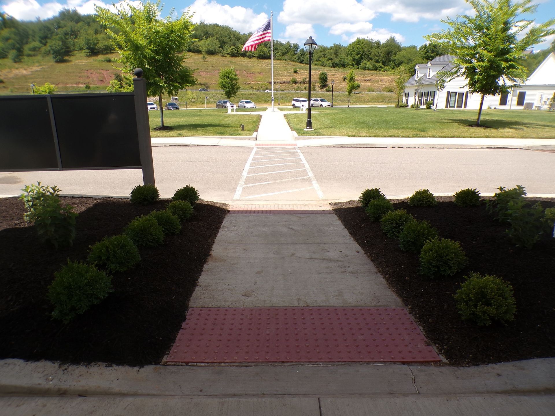 Pathway leading through landscaped entrance toward street and American flag on a sunny day