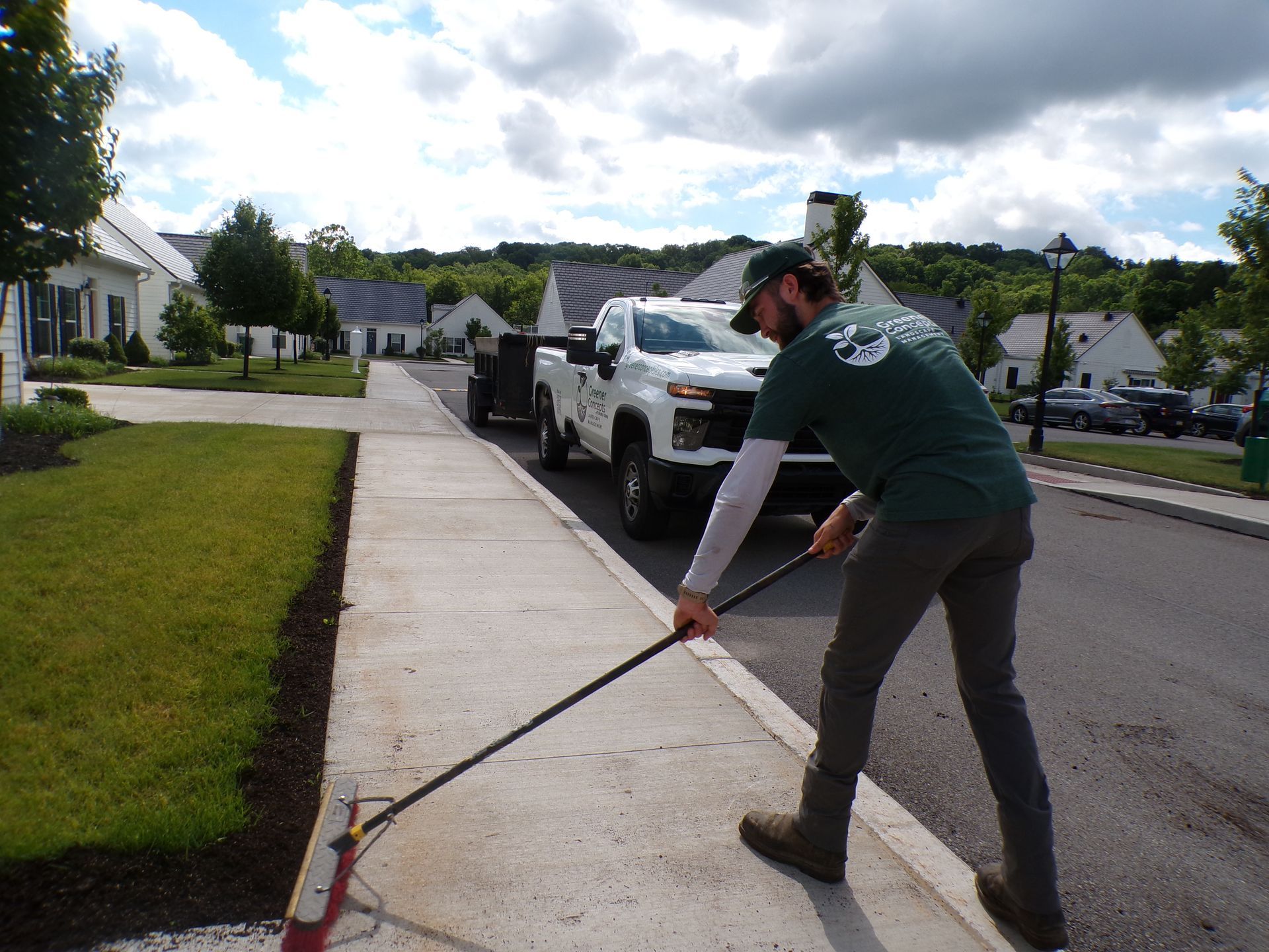 Worker using a long-handled tool beside a white truck on a suburban street