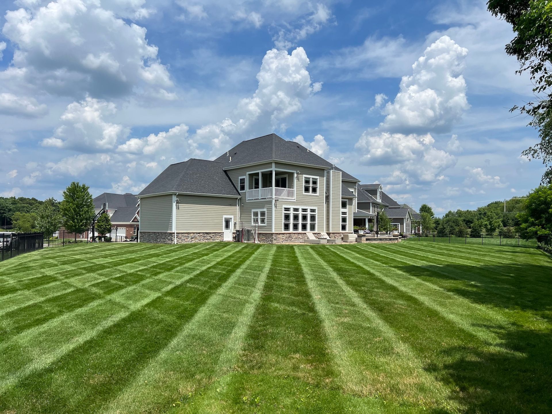 Large suburban house with gray siding and striped green lawn under a partly cloudy blue sky