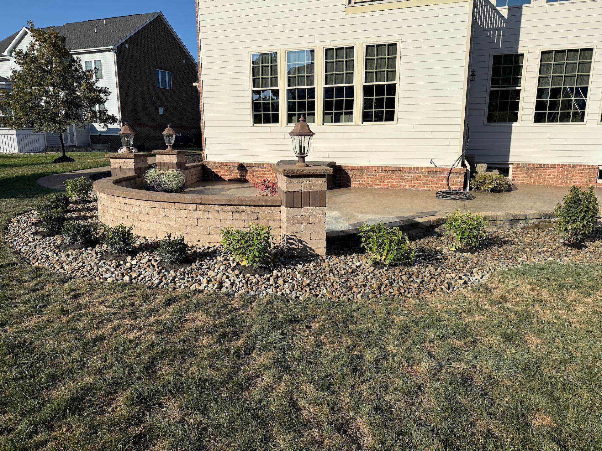 Front yard landscaping with stone planter wall, shrubs, and a white house facade