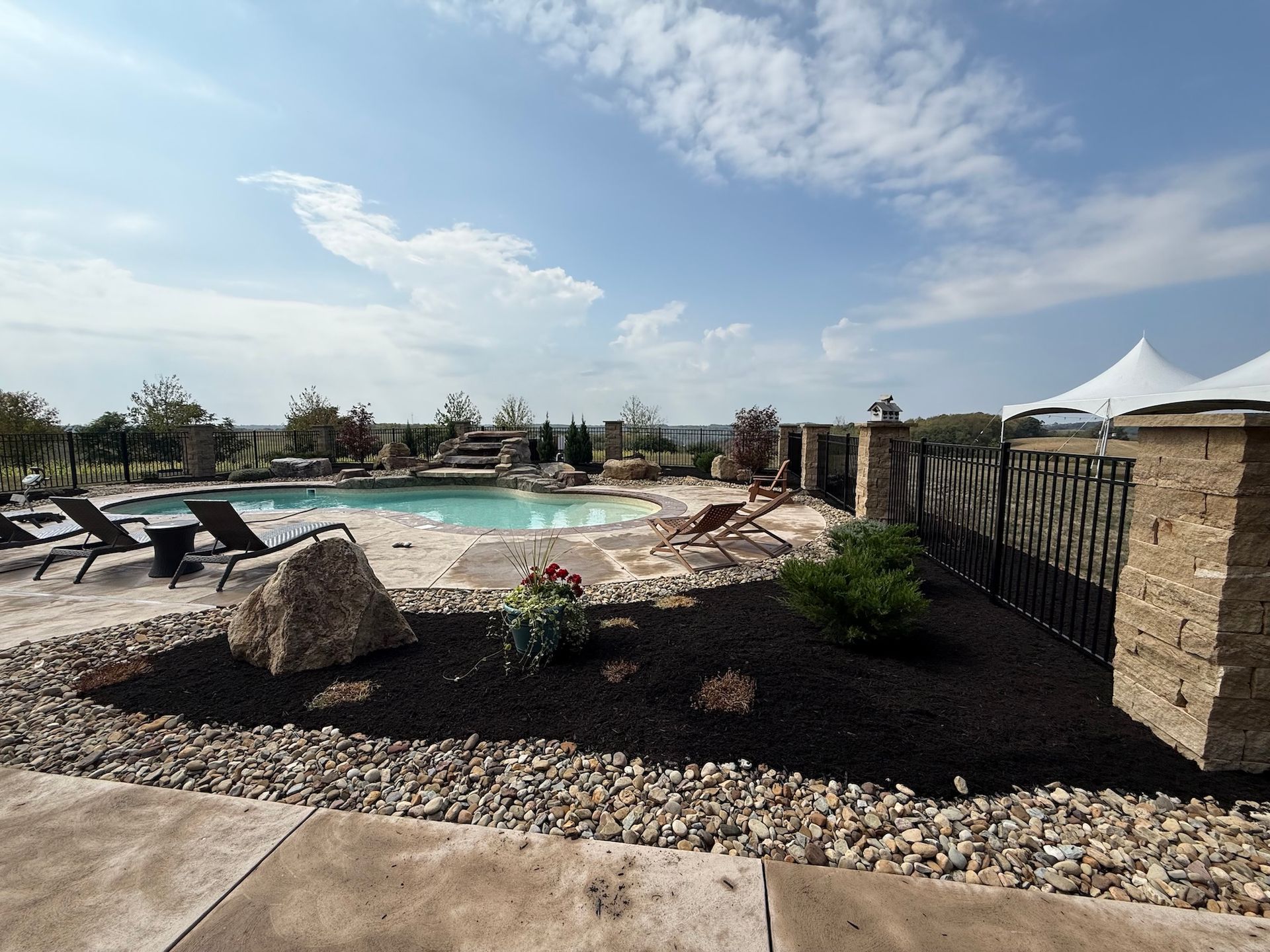 Outdoor pool with lounge chairs, rock landscaping, and white tents under a blue sky