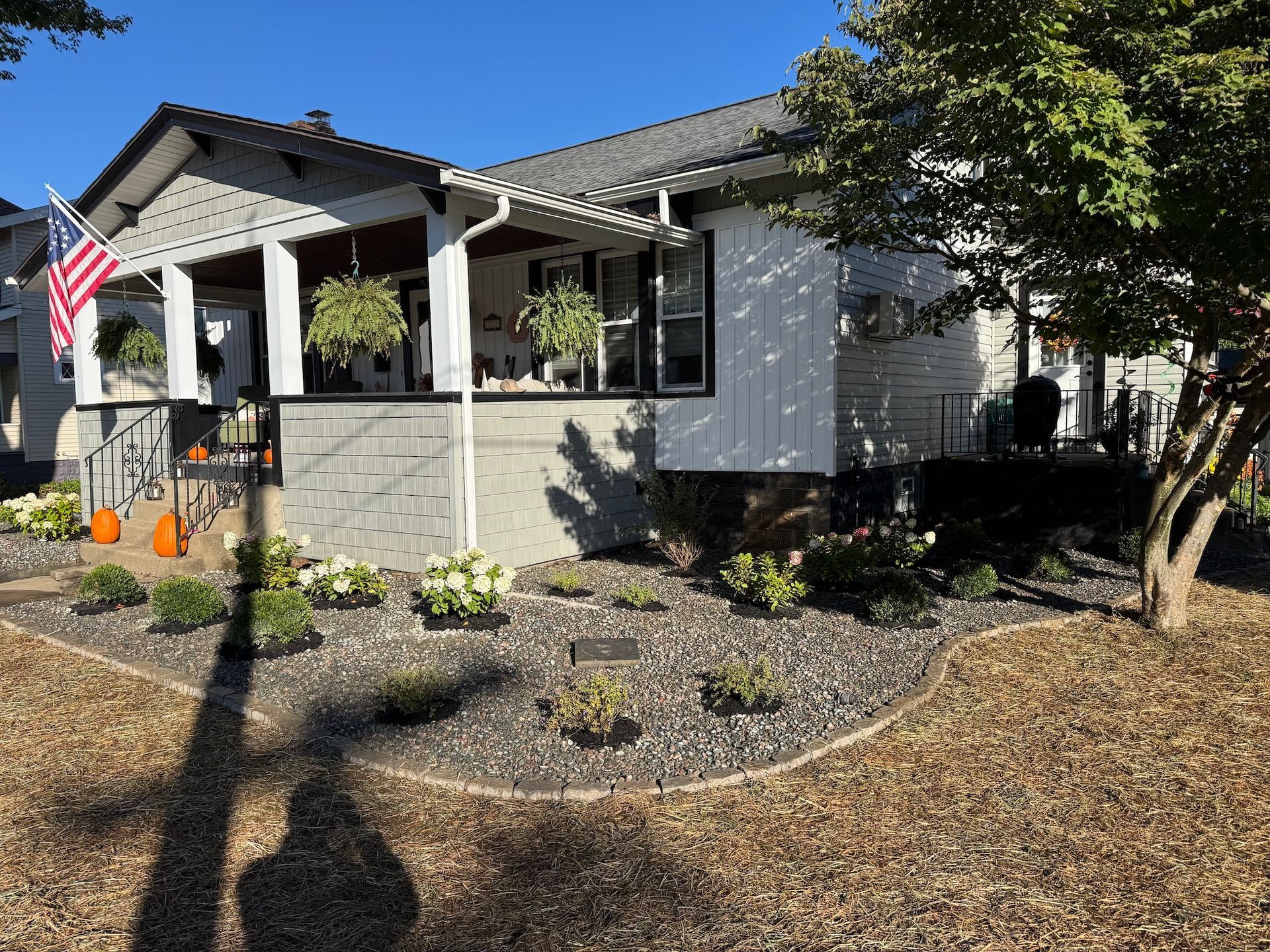 Gray house with front porch, American flag, and landscaped yard with mulch and shrubs.