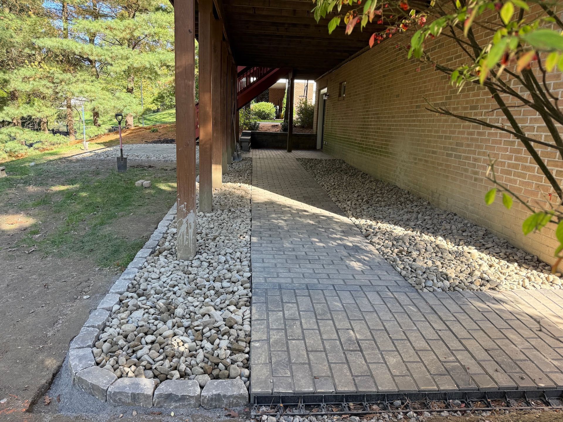 Brick walkway beside a covered brick wall, bordered by white gravel and supported by wooden posts.