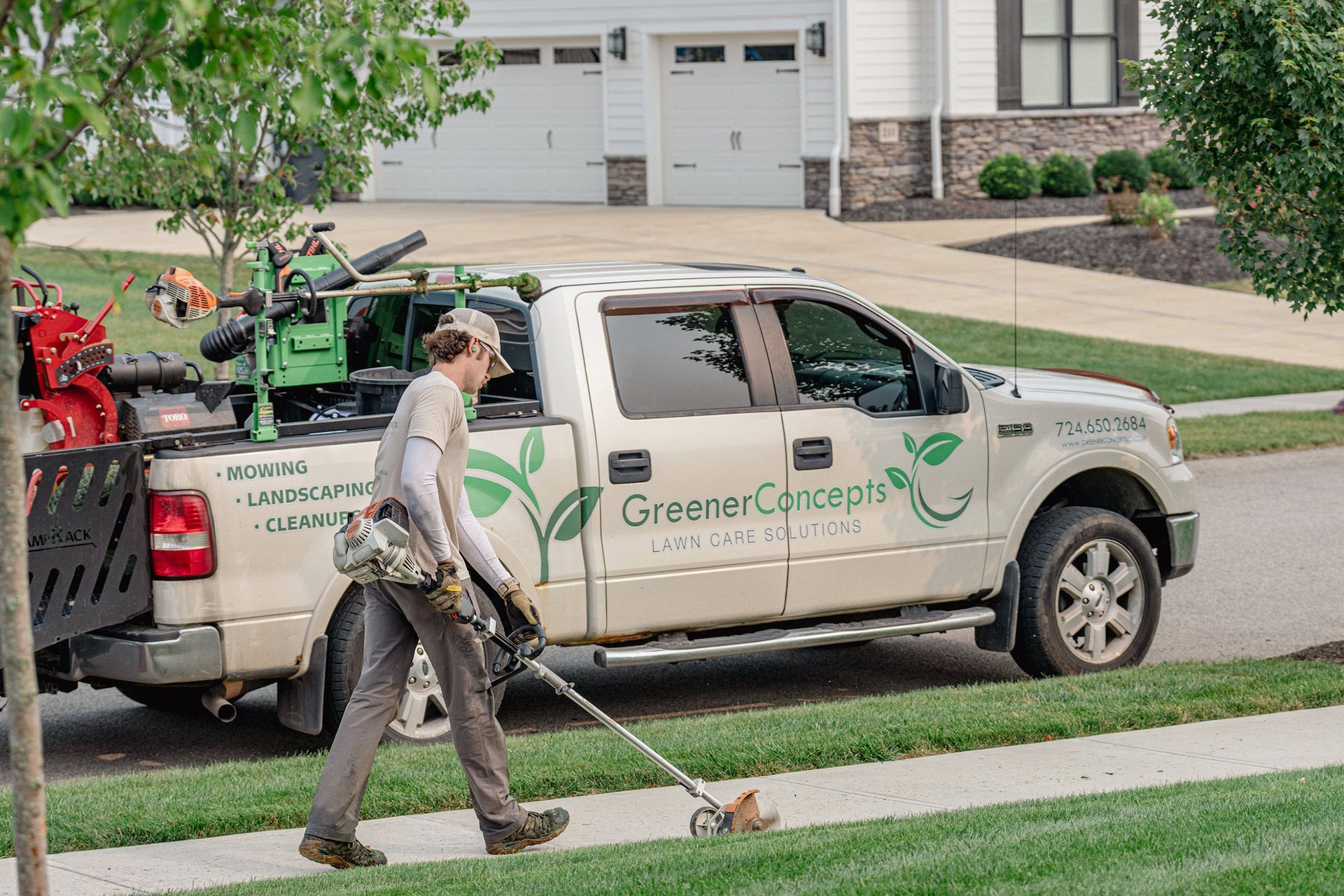 Green Care lawn service worker walking beside a truck on a suburban street.