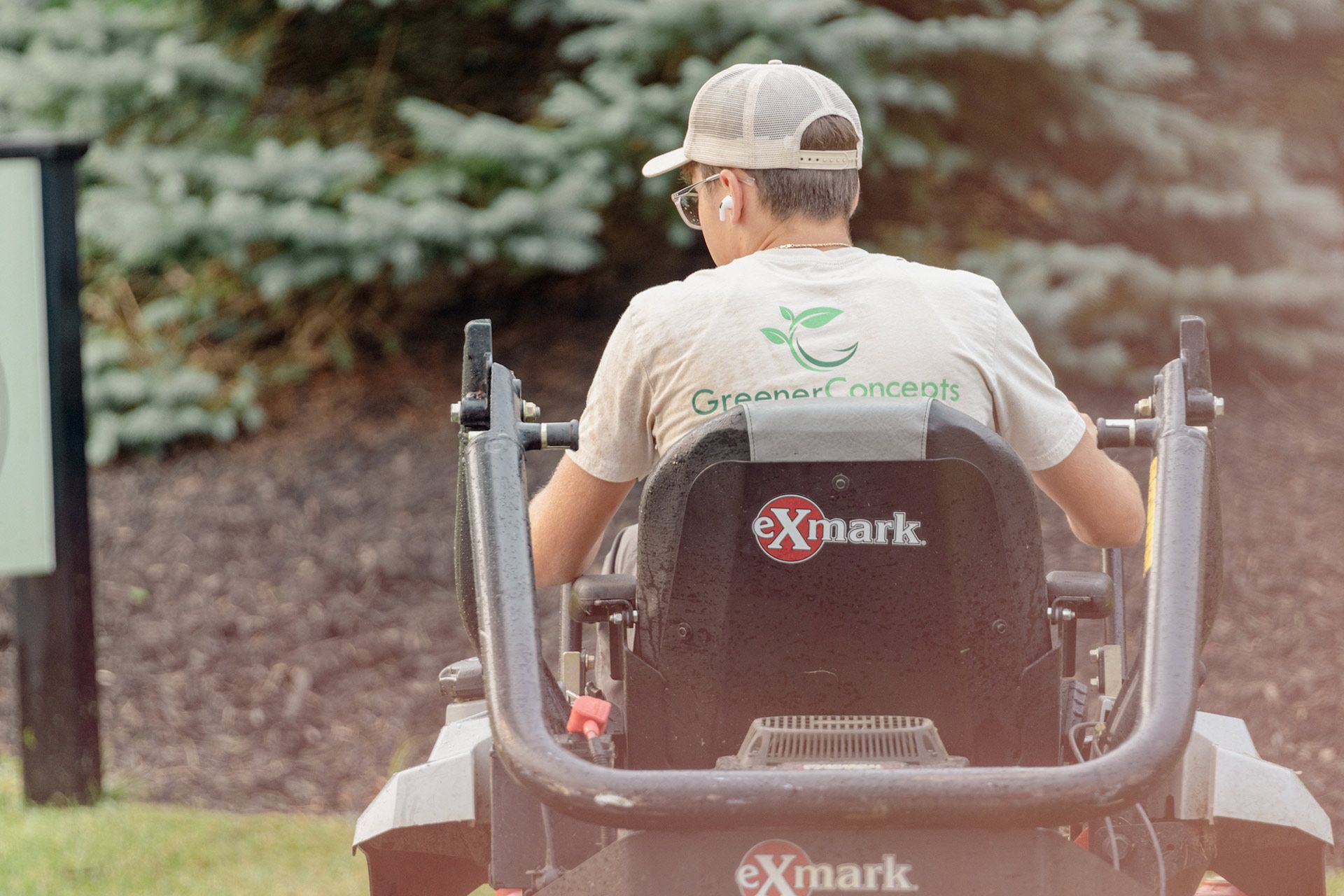 Man seated on an Exmark mower driving through a landscaped area, viewed from behind