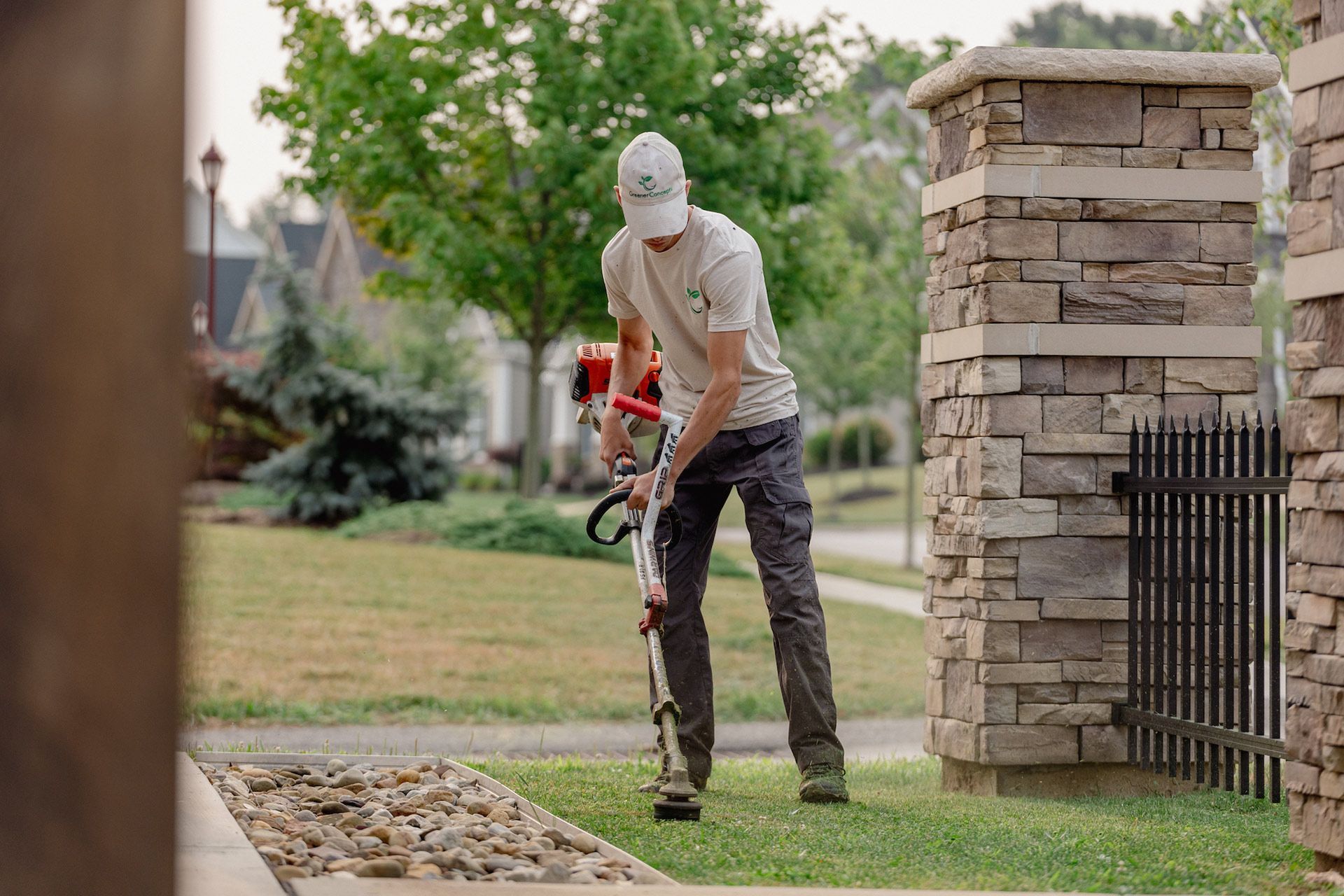 Person using a string trimmer near a stone pillar in a suburban yard