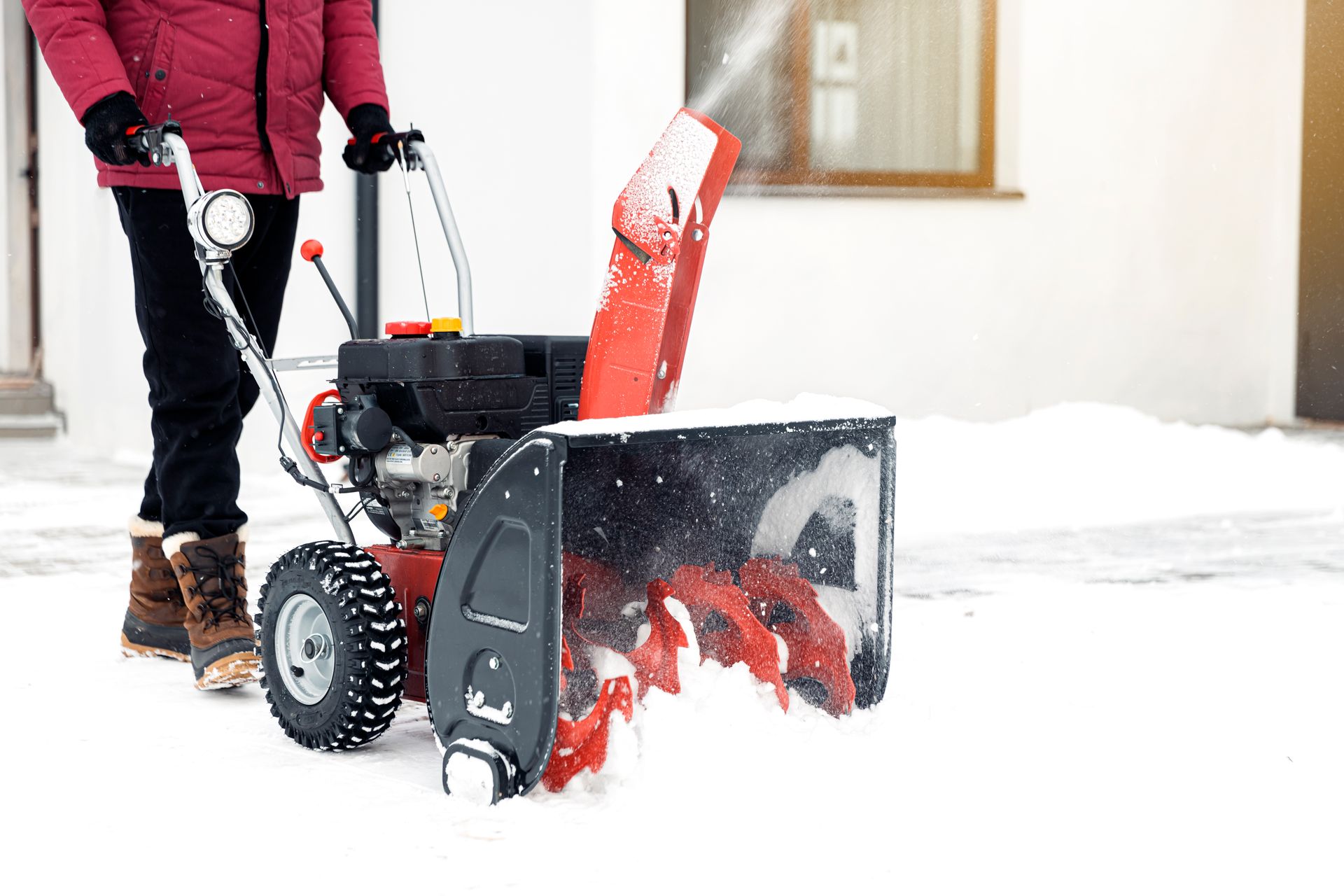 Person operating a red snow blower to clear snow from a driveway
