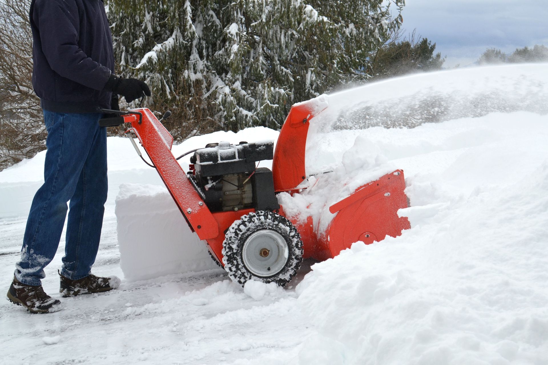 Person using a red snow blower to clear deep snow outdoors