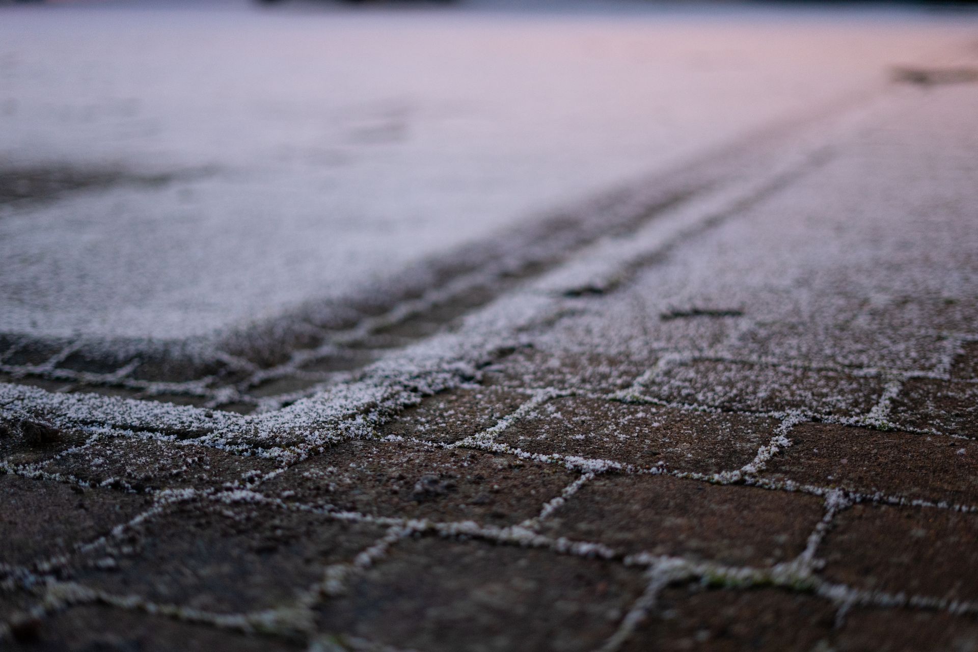 Snow-dusted brick pavement with a diagonal curb line in soft, blurry light