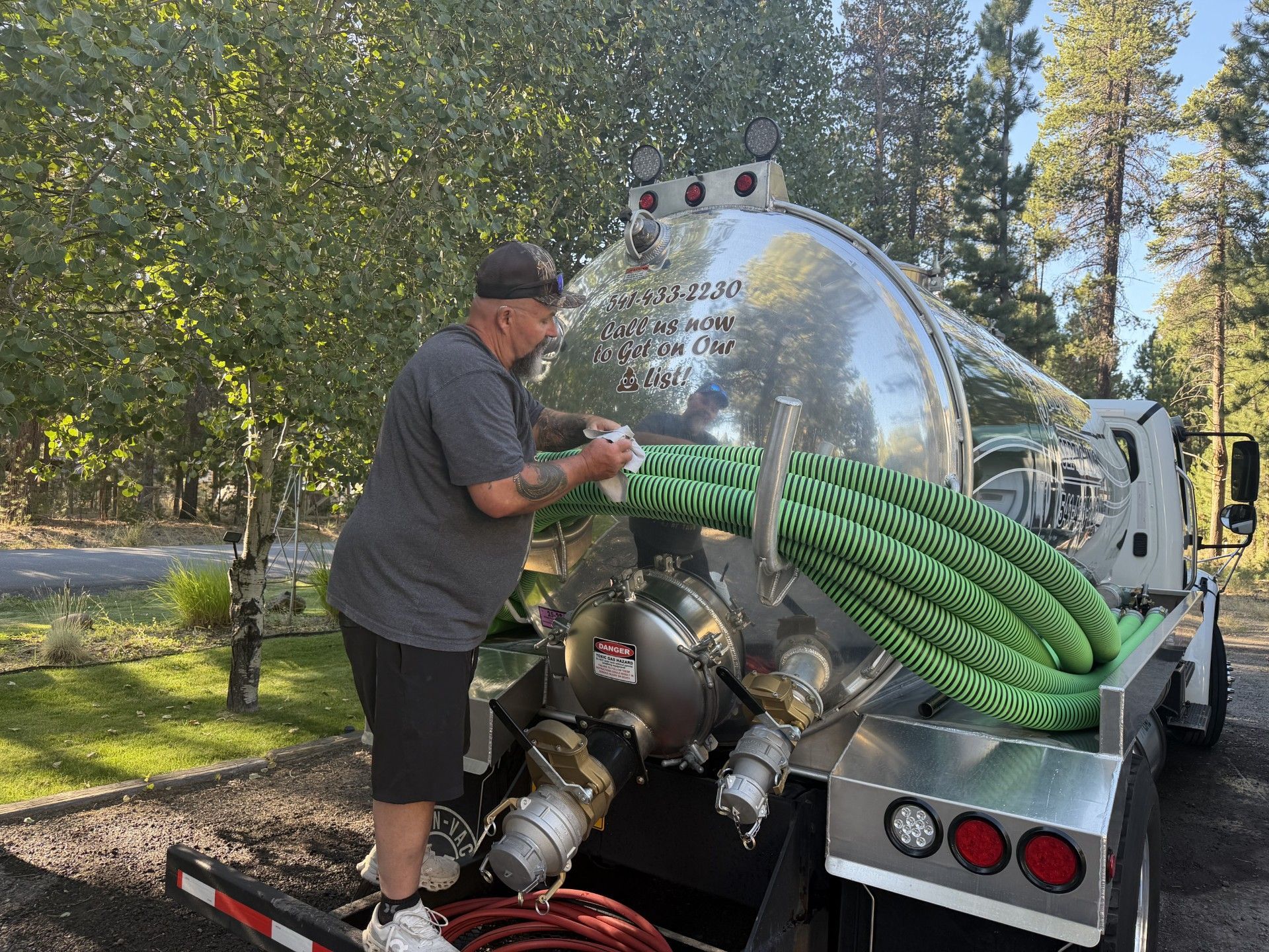 Worker loading green hose onto a water tank truck in a wooded outdoor area