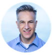 Paul DelGrosso Man in a blue button-down shirt smiles; gray hair, light blue background.
