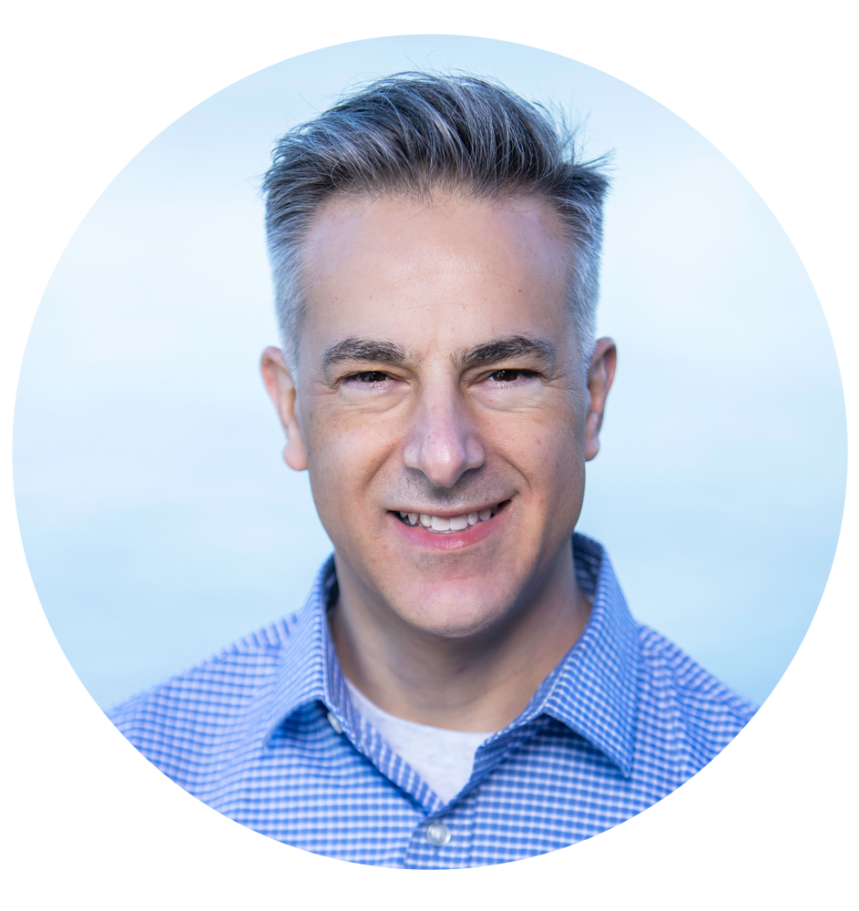 Man in a blue button-down shirt smiles; gray hair, light blue background.
