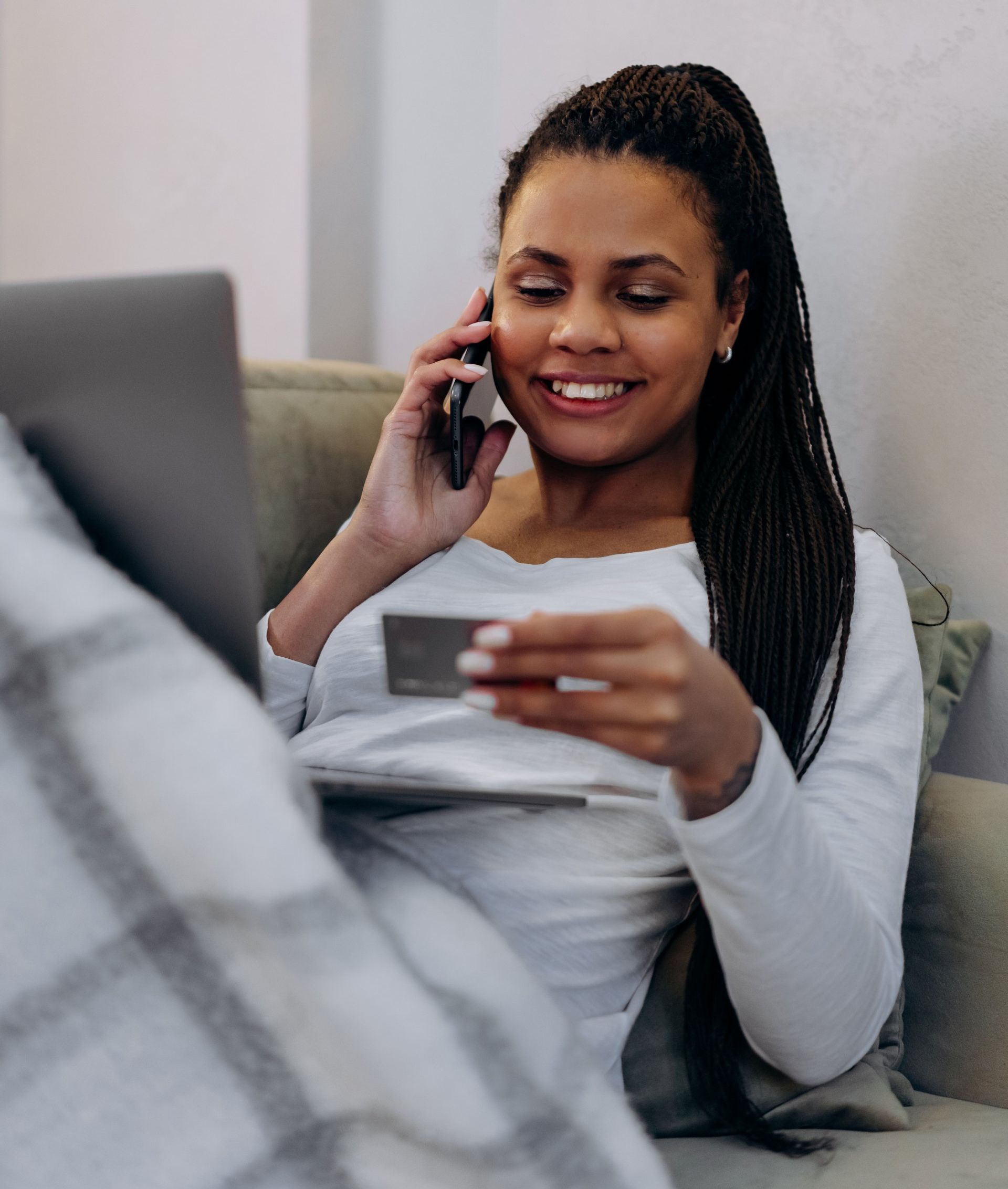 A woman is sitting on a couch talking on a cell phone while holding a credit card.